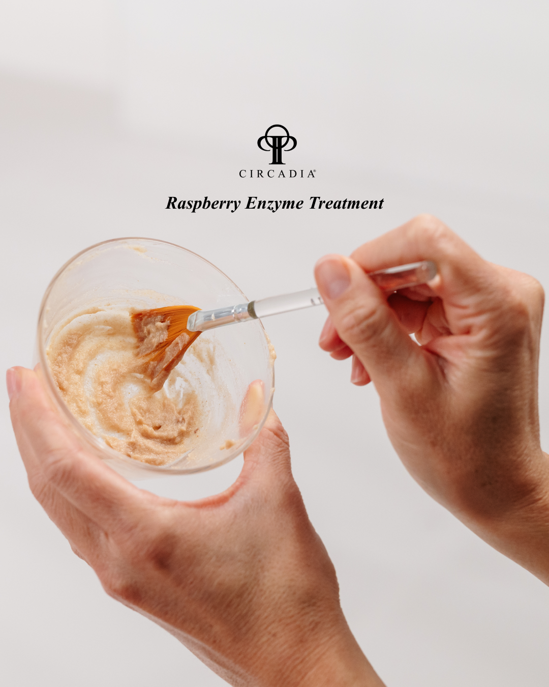 Hands preparing a raspberry enzyme treatment with a brush inside a glass container, with text indicating a brand called Circadia and a treatment for raspberry enzyme.