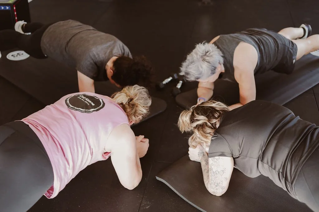 Four women doing planks on exercise mats in a gym.