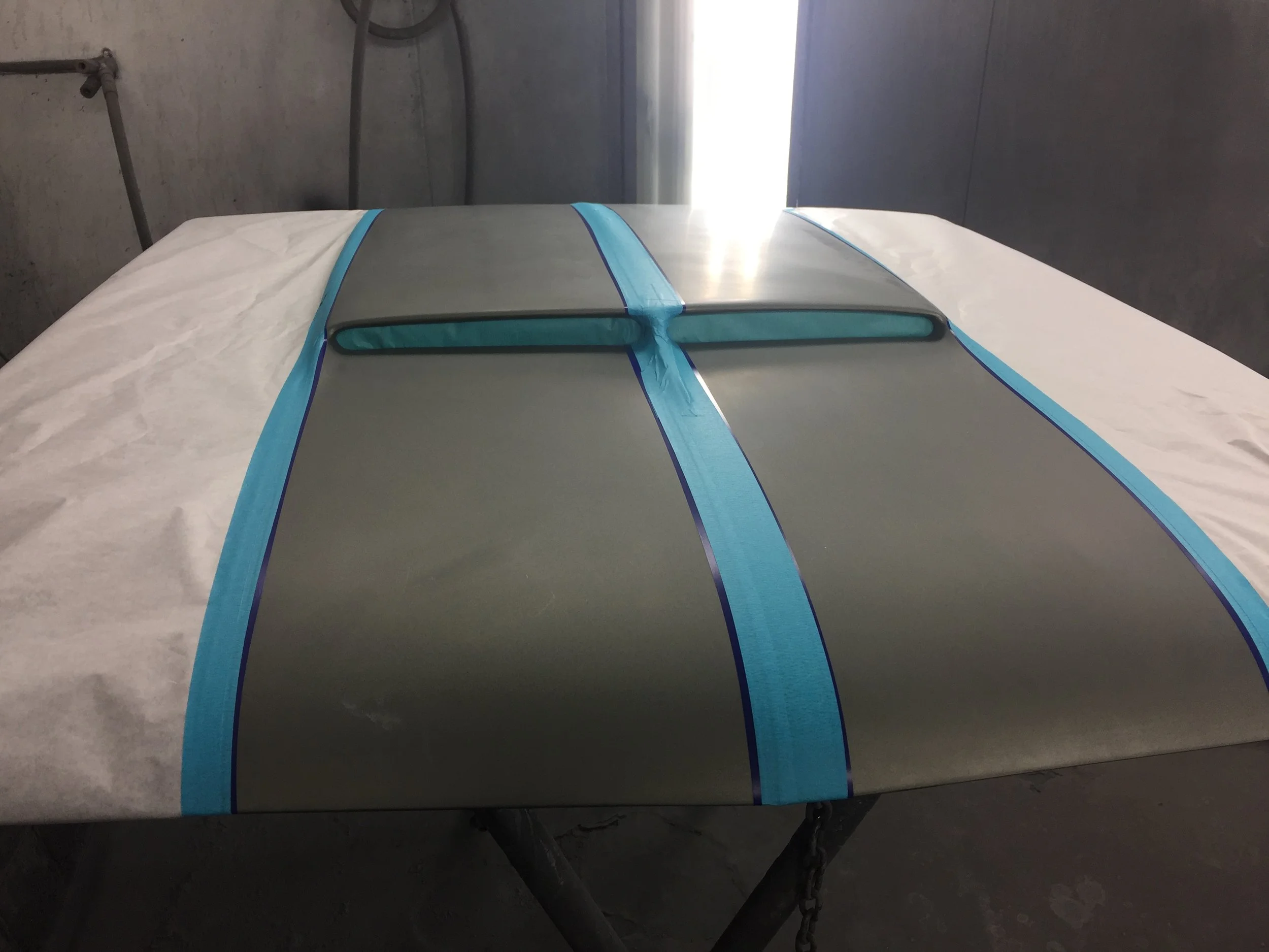 A work table with a large sheet of metal and blue painter's tape forming a pattern on a dark gray surface.