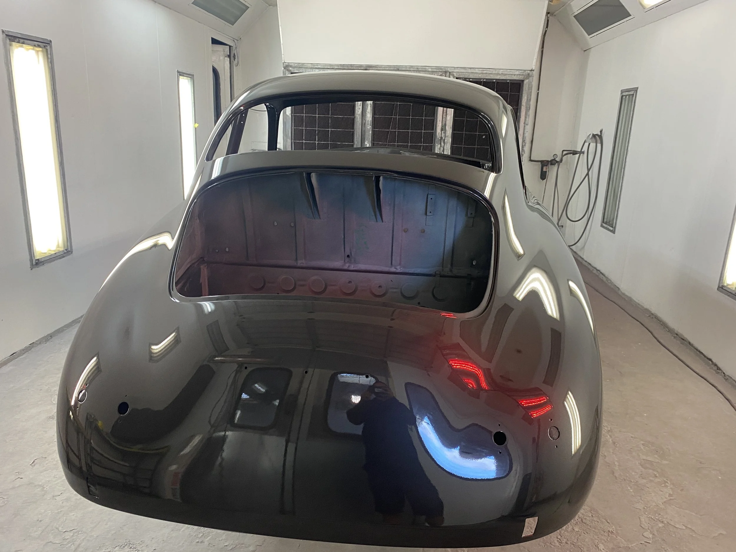 Front view of a shiny, dark-colored vintage car inside a white-walled garage.