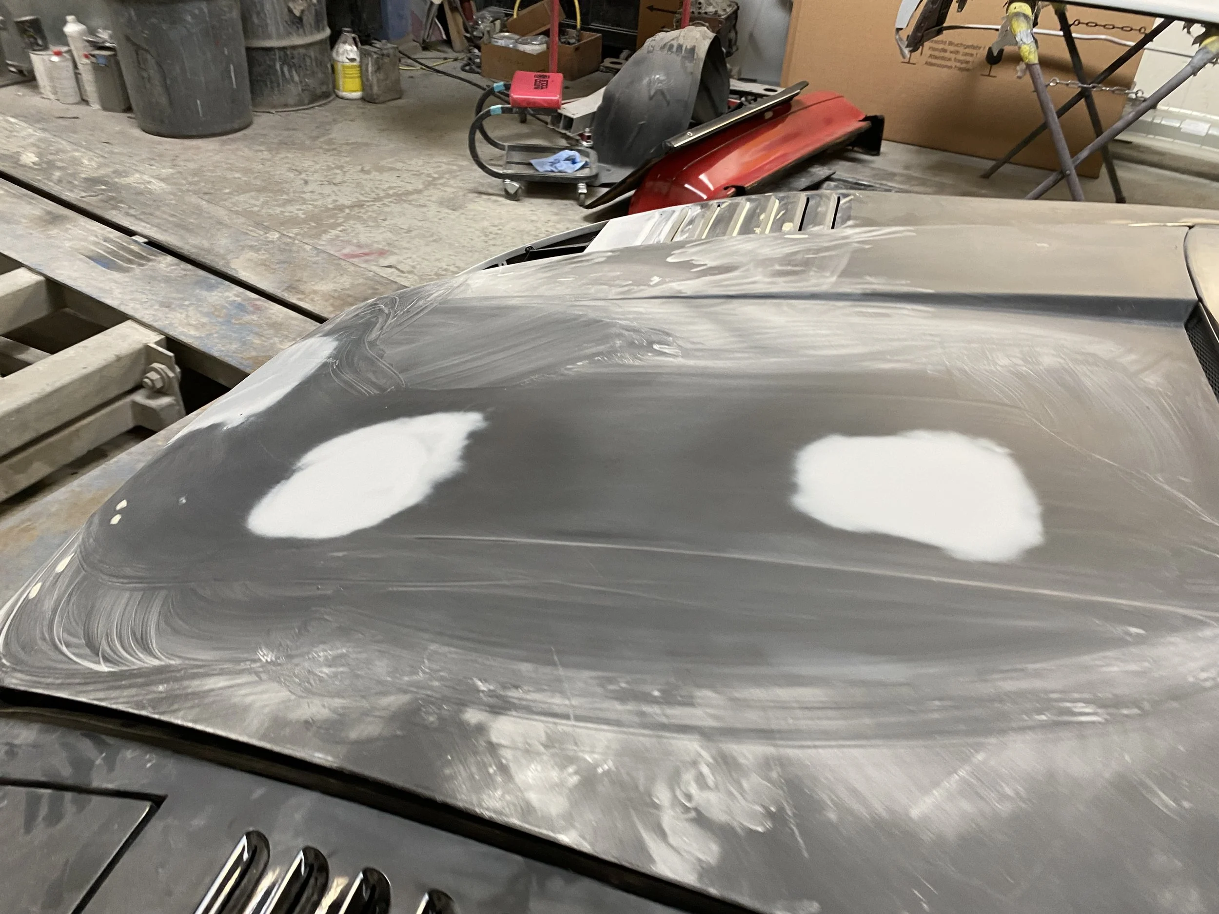 Close-up of a car hood undergoing bodywork repair, with patches of filler material visible on the surface.