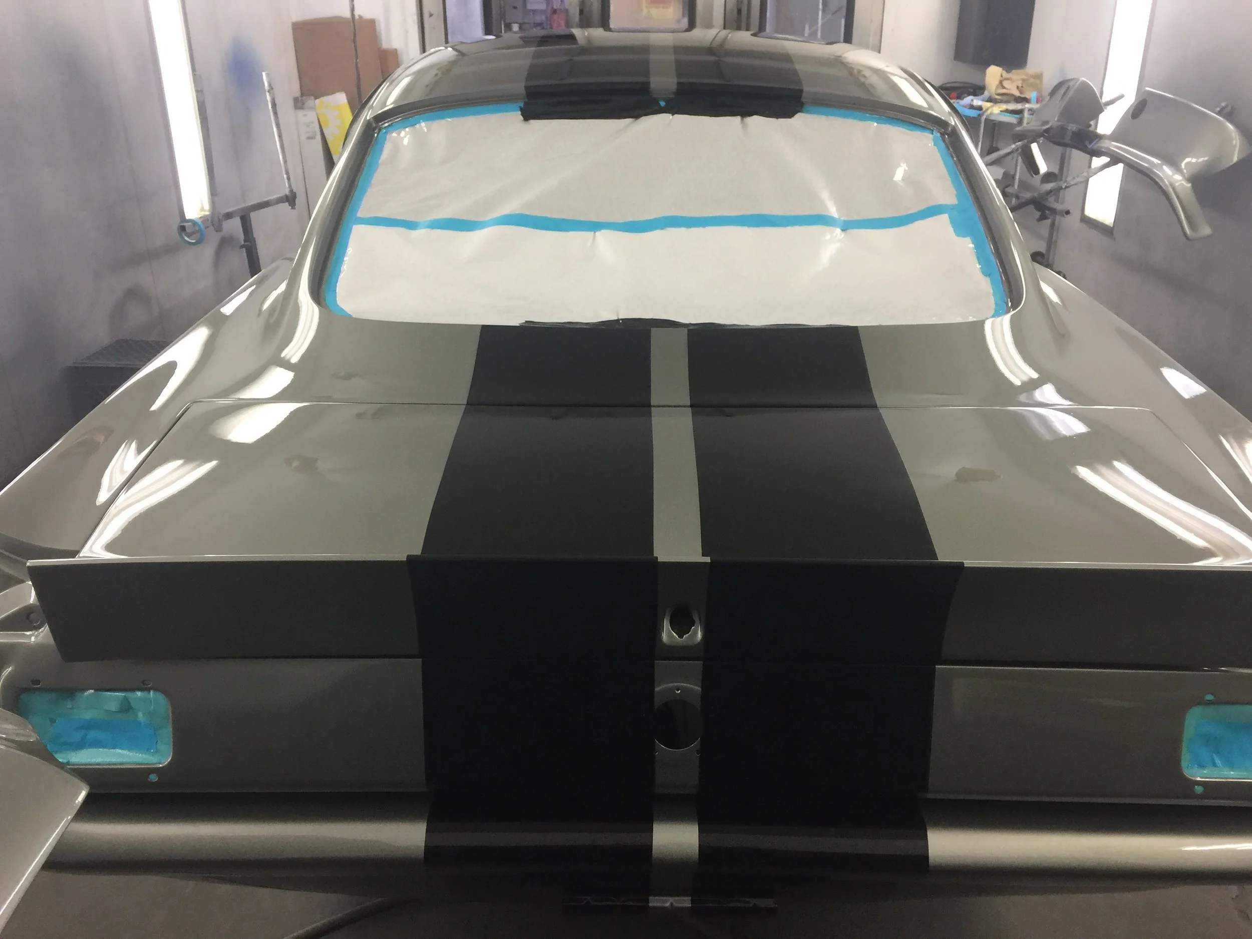 Front view of a car inside a workshop, with masking paper and blue tape on the windshield, preparing for painting or detailing.