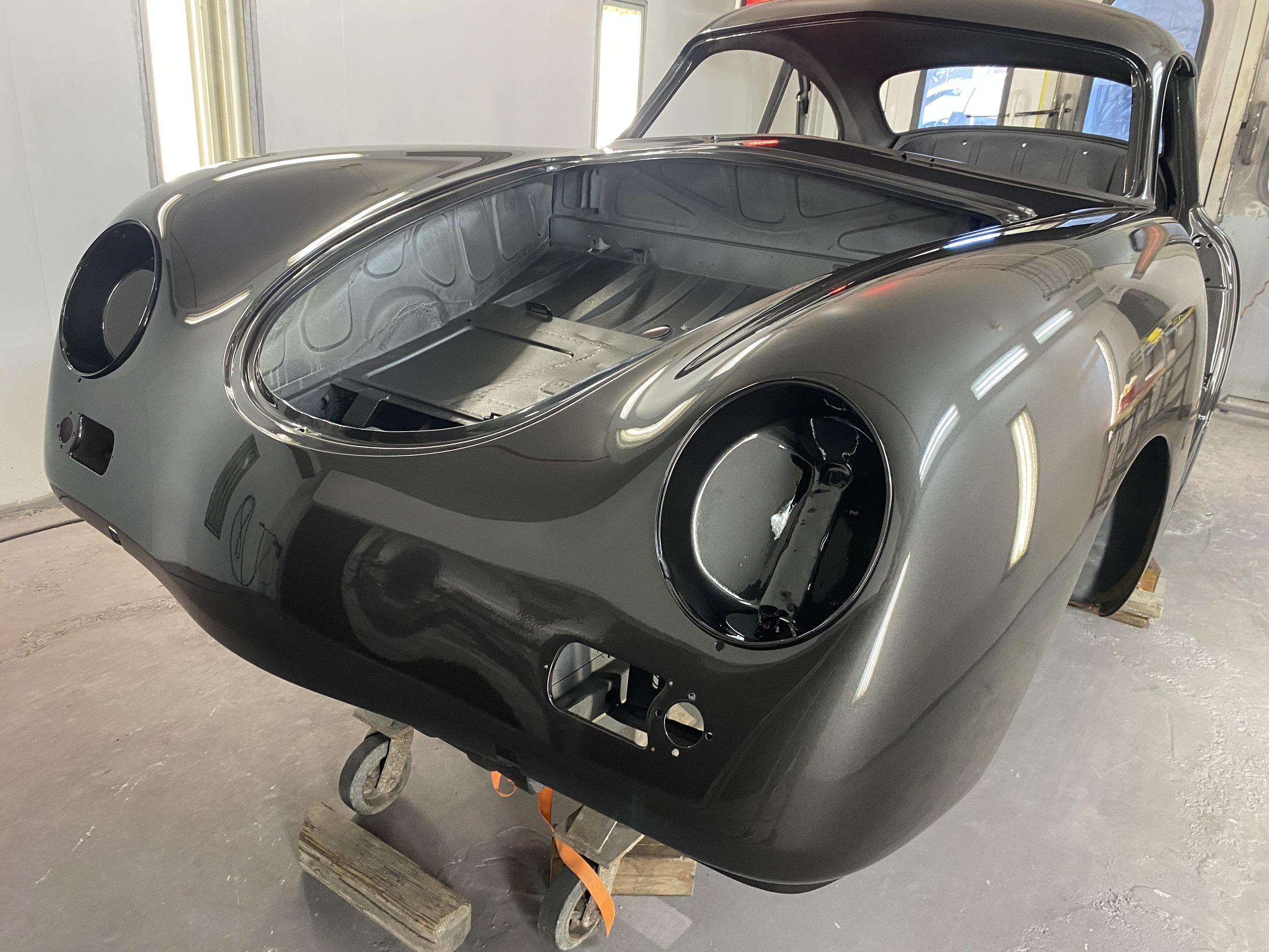 A vintage race car body shell in black with no windows, headlights, or interior, on a wooden platform in a garage or workshop.