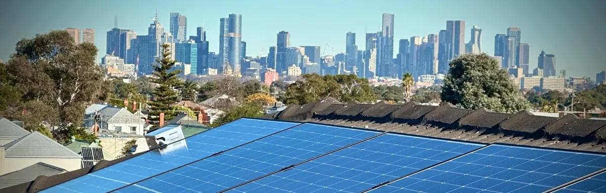 View of solar panels on a rooftop with a city skyline in the background, featuring tall skyscrapers and lush trees in a clear day.