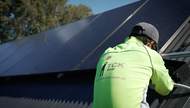 A worker in a neon yellow TCK Solar shirt installing or maintaining solar panels on a solar energy system.