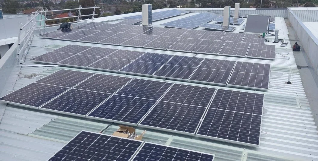 Array of solar panels installed on a rooftop, with some equipment and railing visible.