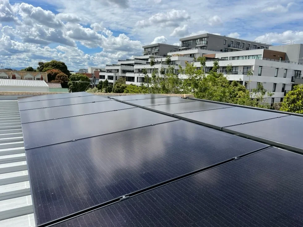 Solar panels installed on a building roof with a background of modern apartment buildings and a partly cloudy sky.