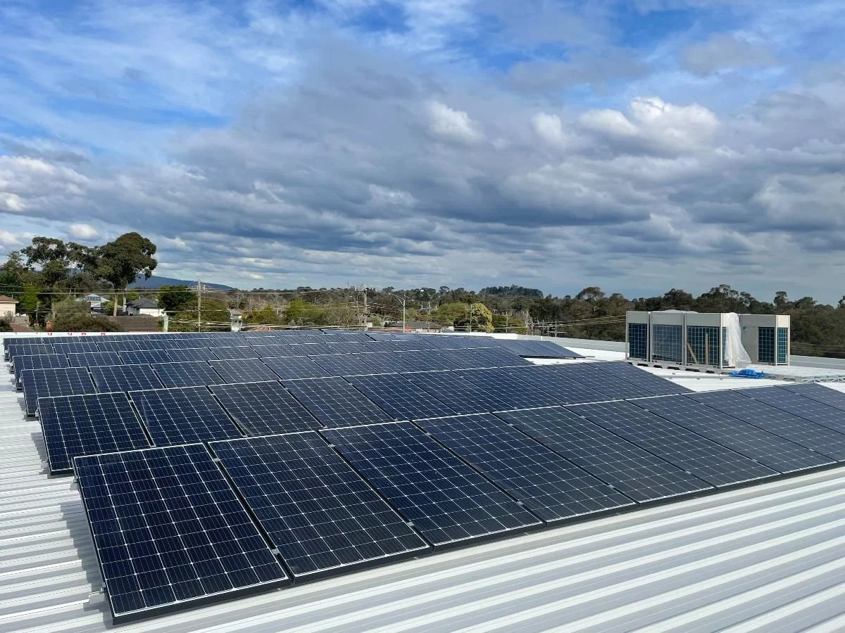 Solar panels installed on a roof with a cloudy sky and trees in the background.