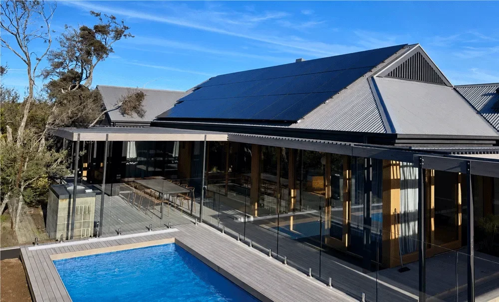 A modern house with solar panels on the roof, a swimming pool, and a deck area enclosed with glass panels.