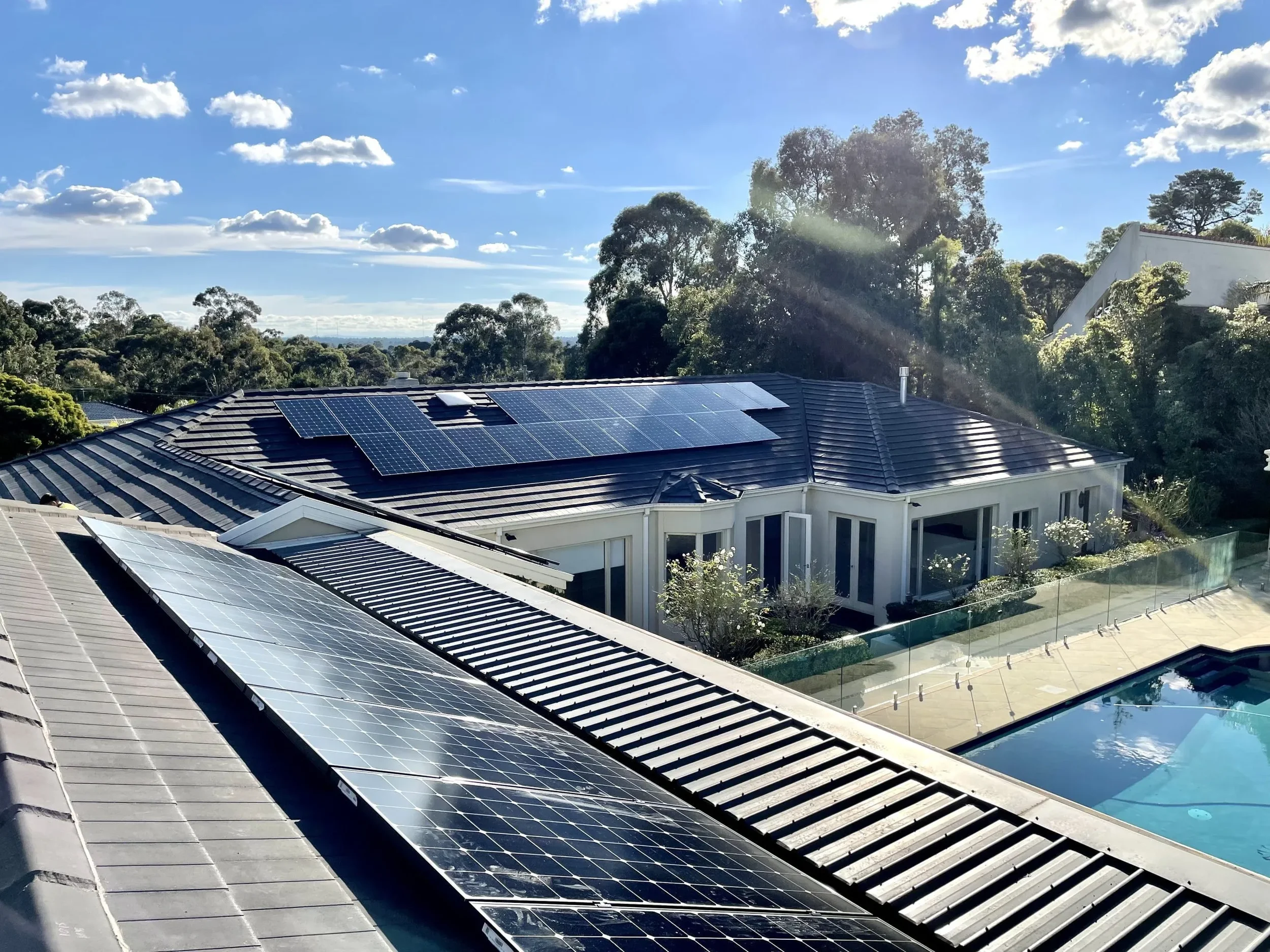 Residential house with solar panels on the roof, surrounded by trees, under a partly cloudy sky.