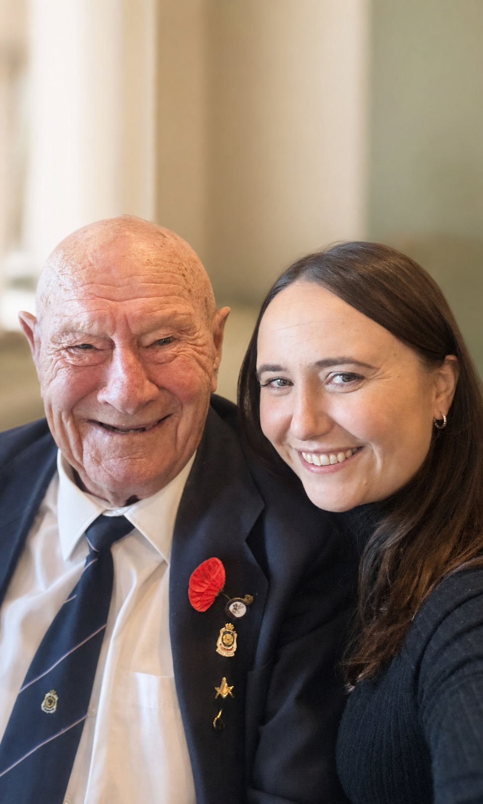 An elderly man and a young woman smiling and taking a selfie together indoors.