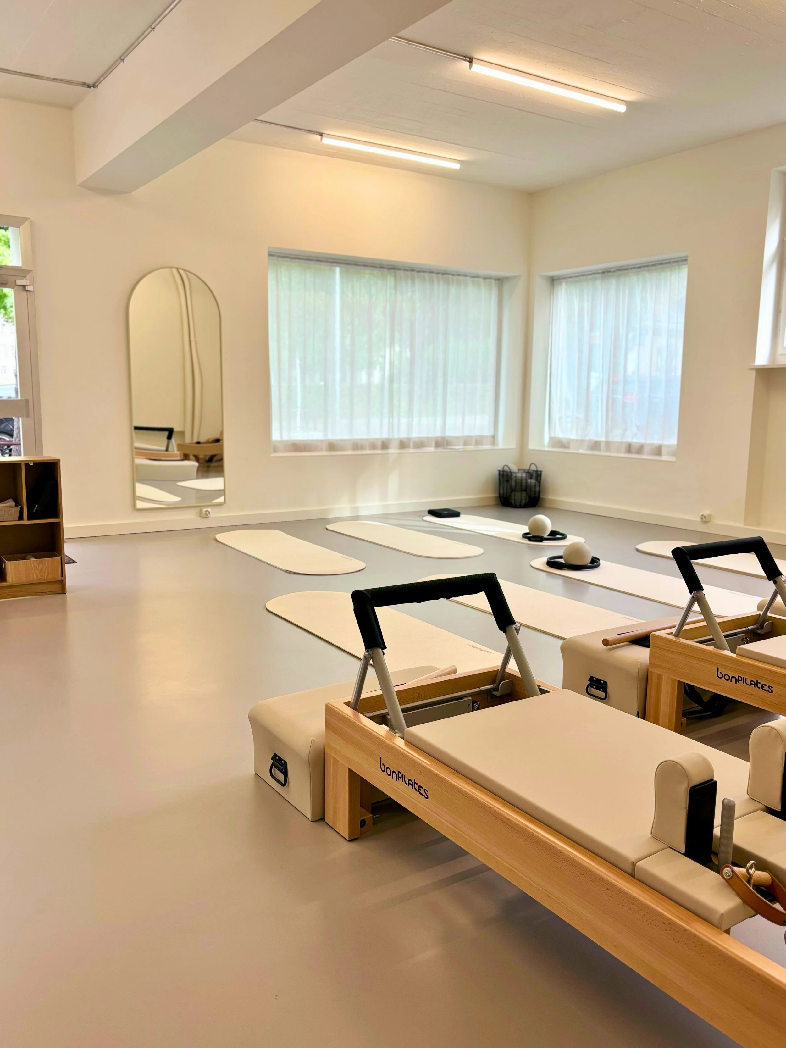 Ein heller, grosser Raum mit Pilates-Geräten, Reformern, und Matten sowie Pilates-Equipment.