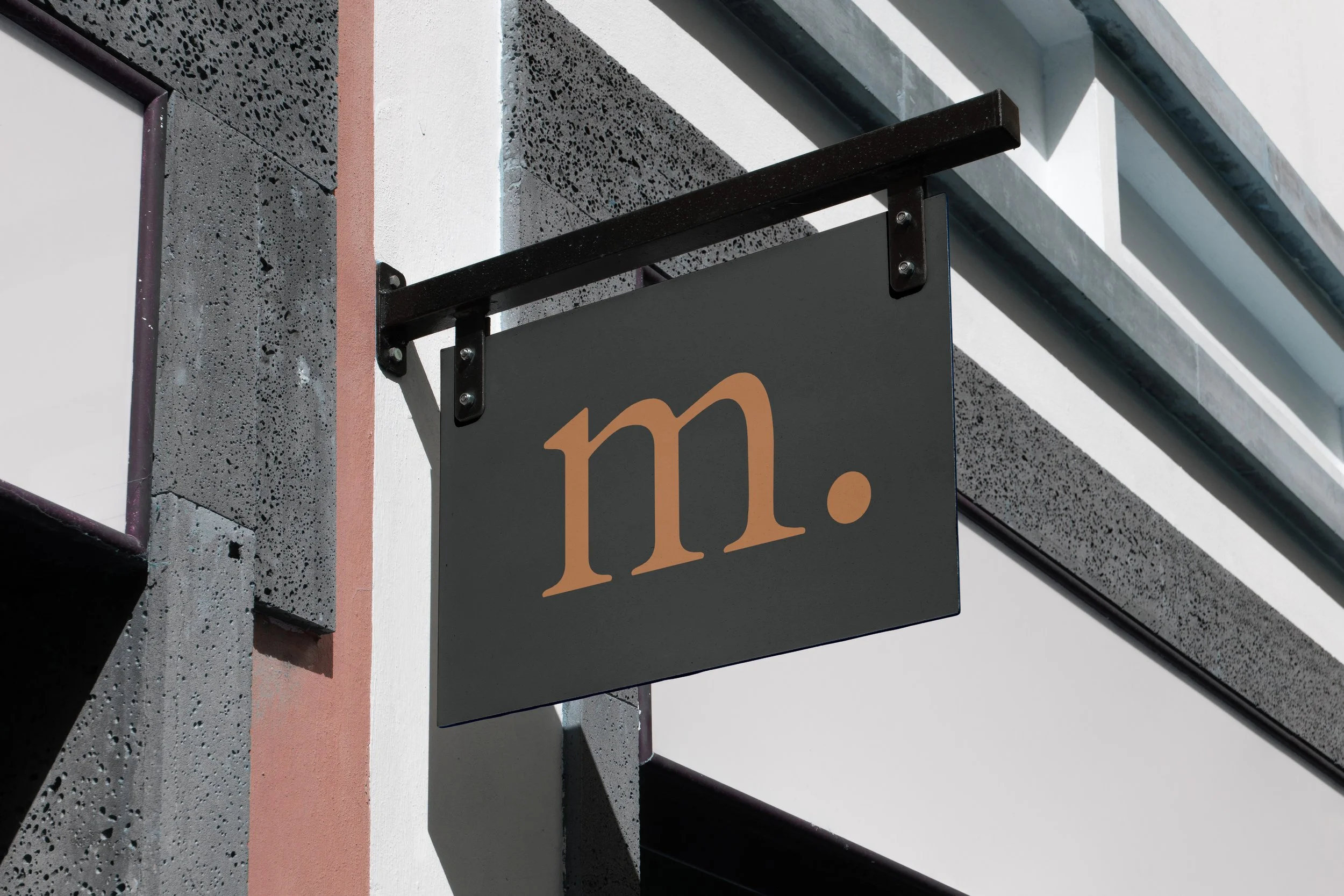 Black hanging sign with an orange stylized logo on a textured stone building facade