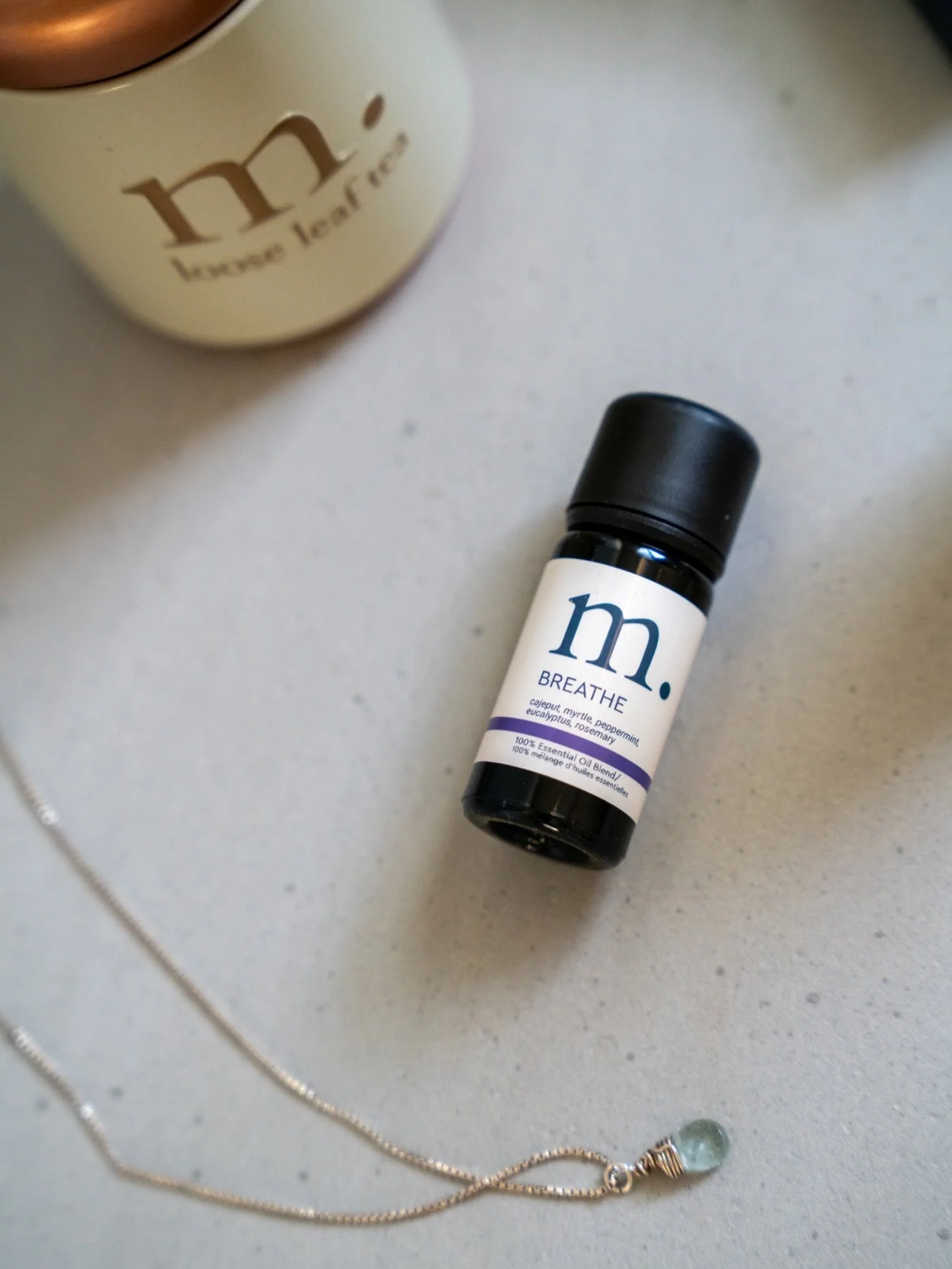 Small bottle of Breathe essential oil blend beside a round container and beaded necklace on a light surface