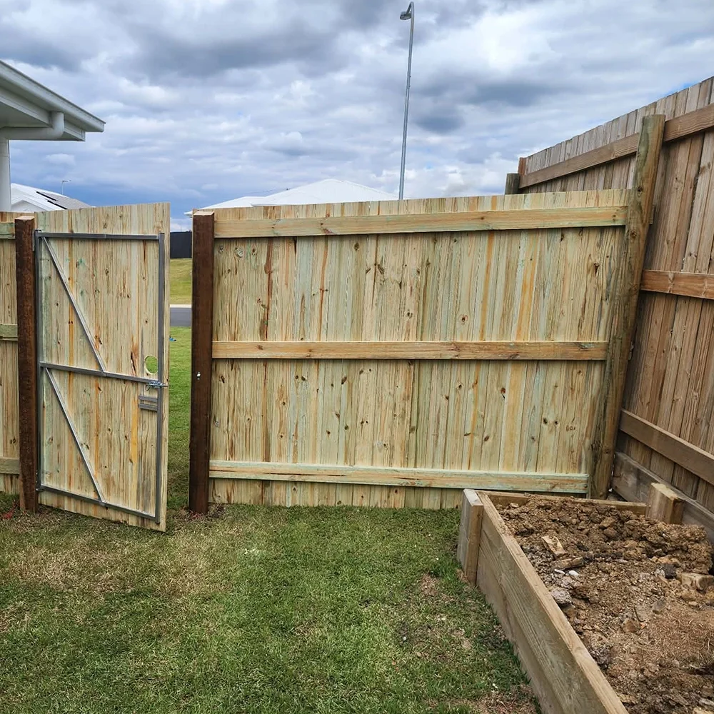 A backyard with a newly built wooden fence and gate, a dirt garden bed, and a cloudy sky overhead.