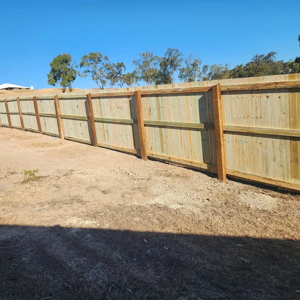 Newly built wooden fence on a dirt ground with clear blue sky and trees in the background.