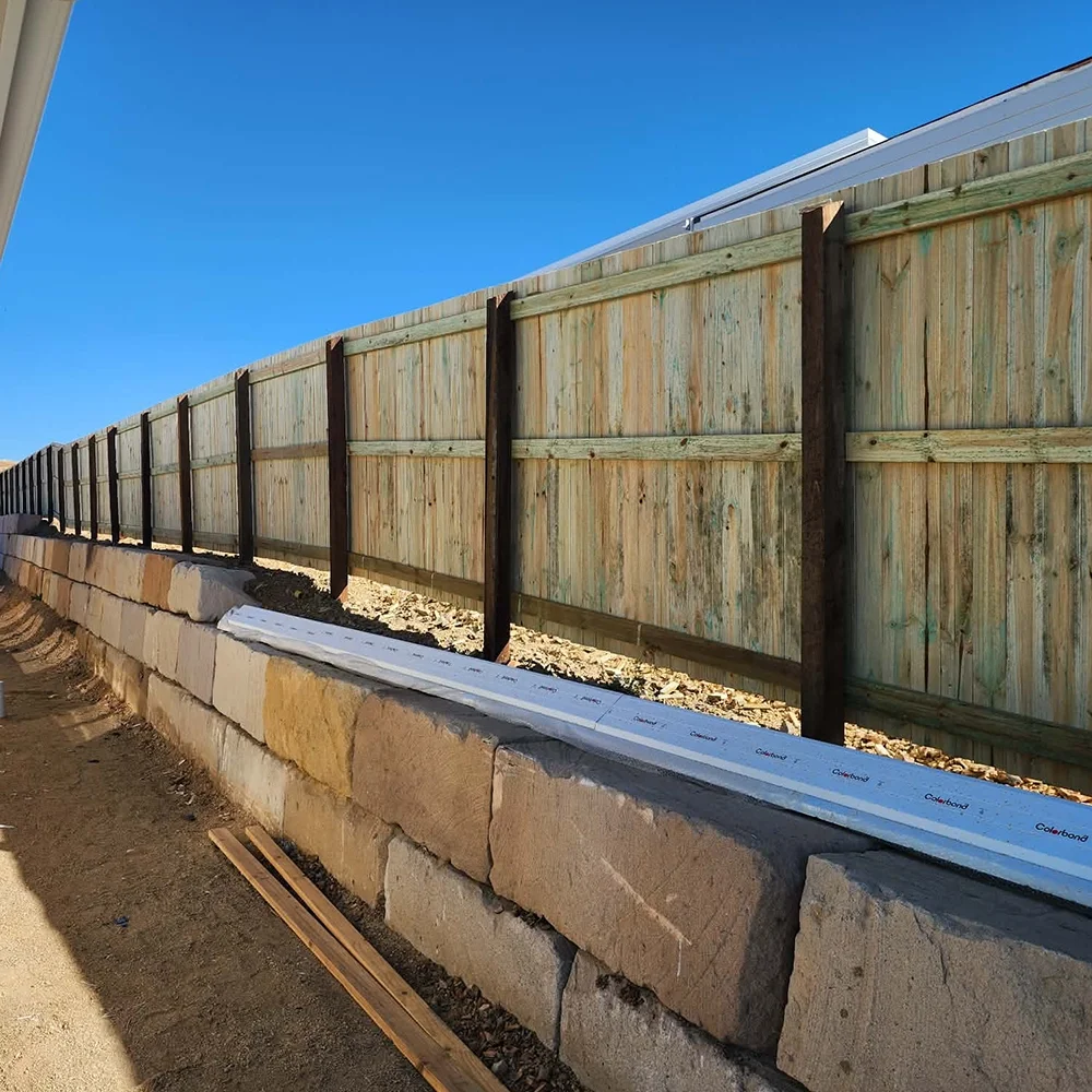 A wooden fence constructed on top of a stone retaining wall, with a blue sky in the background.