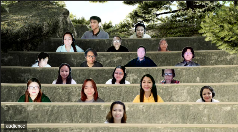 A group of people participating in a virtual outdoor meeting with screens arranged on stone steps in a park-like setting.