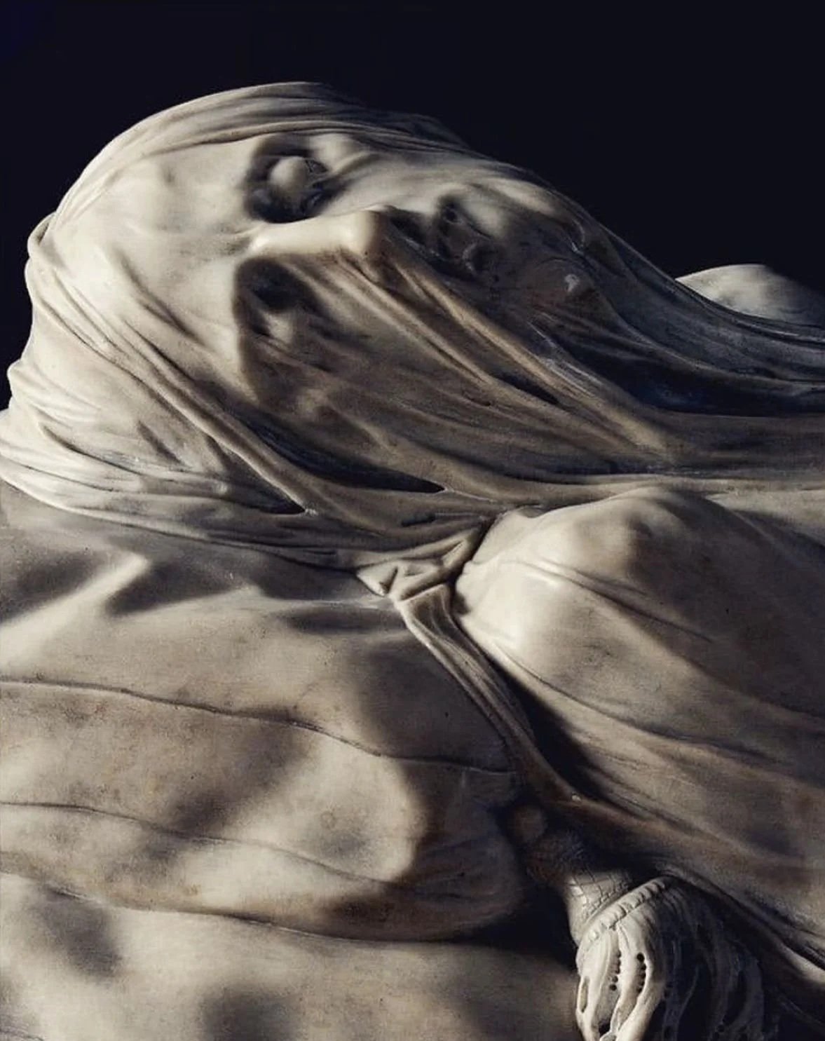 A marble sculpture of a woman with flowing hair, her face turned to the side with a serene expression, against a dark background.