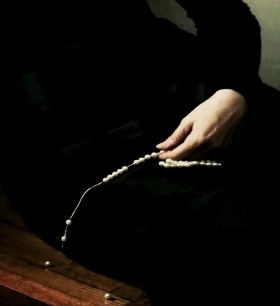 A hand holding a string of white prayer beads over a dark surface.