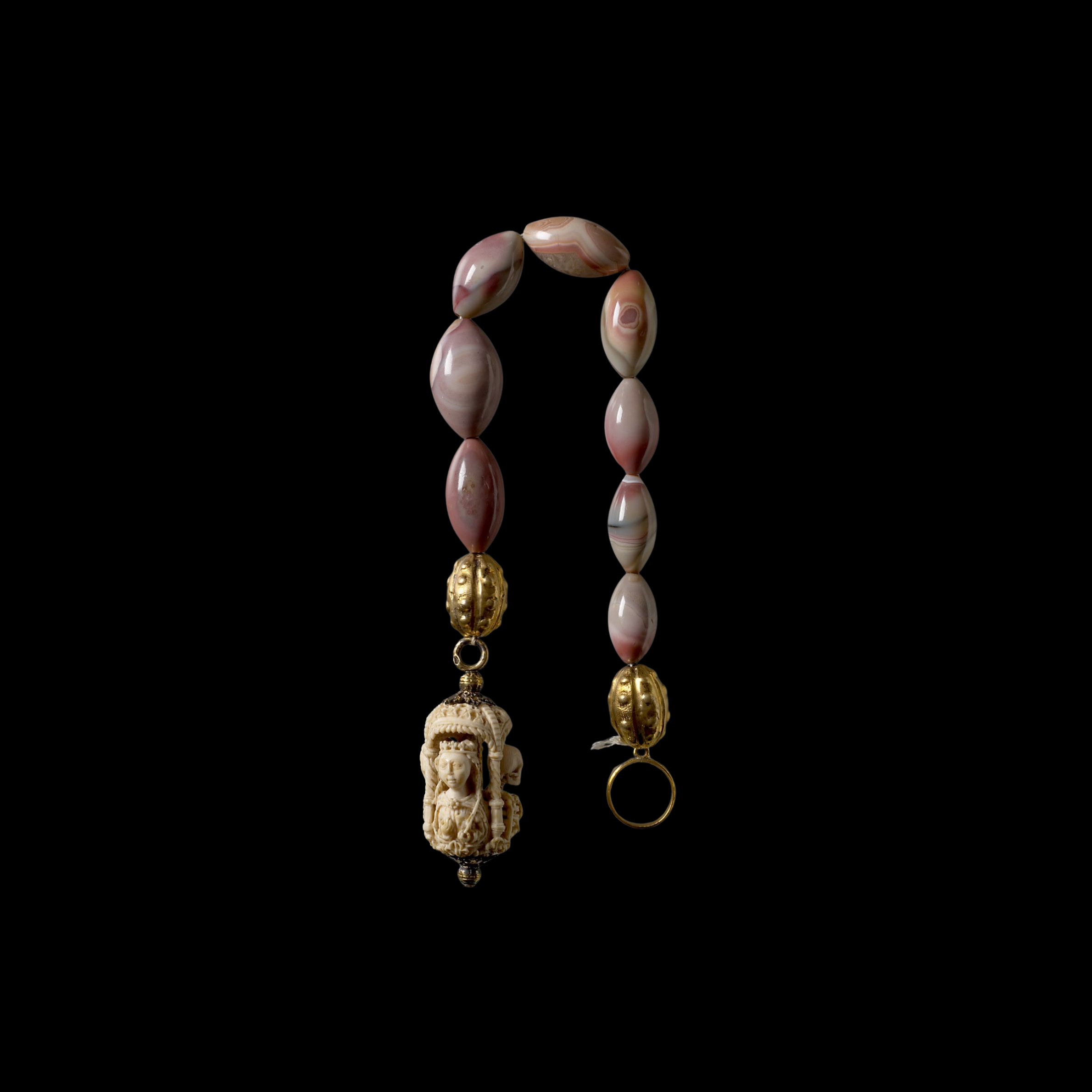 Necklace with various beads and charms, including carved ivory figures and gold details, hanging against a black background with its reflection visible.