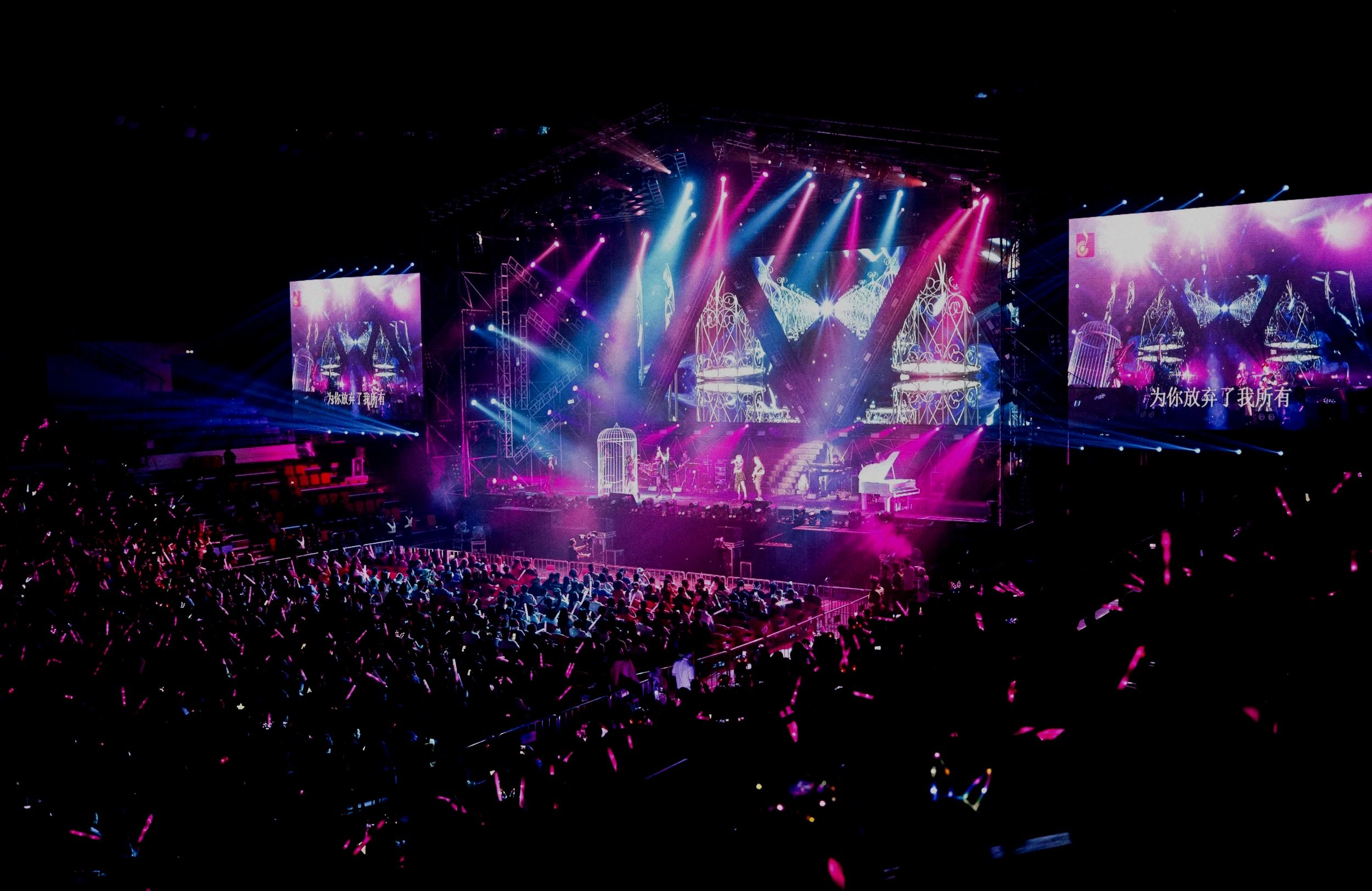 A concert stage with colorful lights, large screens, and an audience with glow sticks at night.