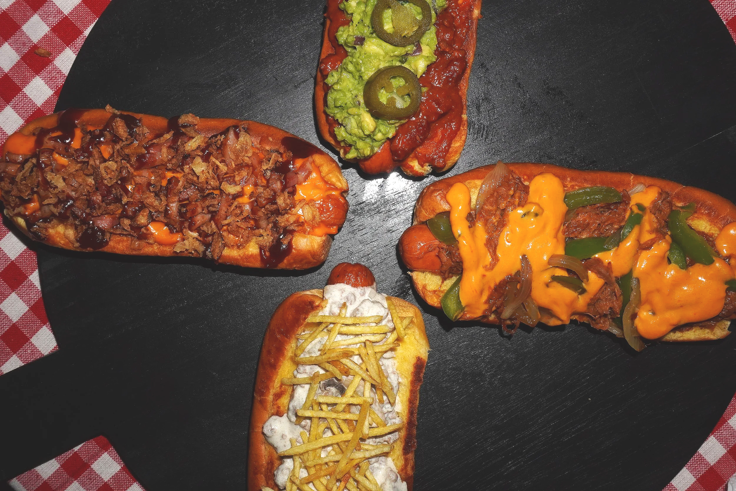 Varios tacos con diferentes ingredientes en un plato de piedra negra, en un fondo de cubrebocas, servilleta de cuadros rojos y blancos.