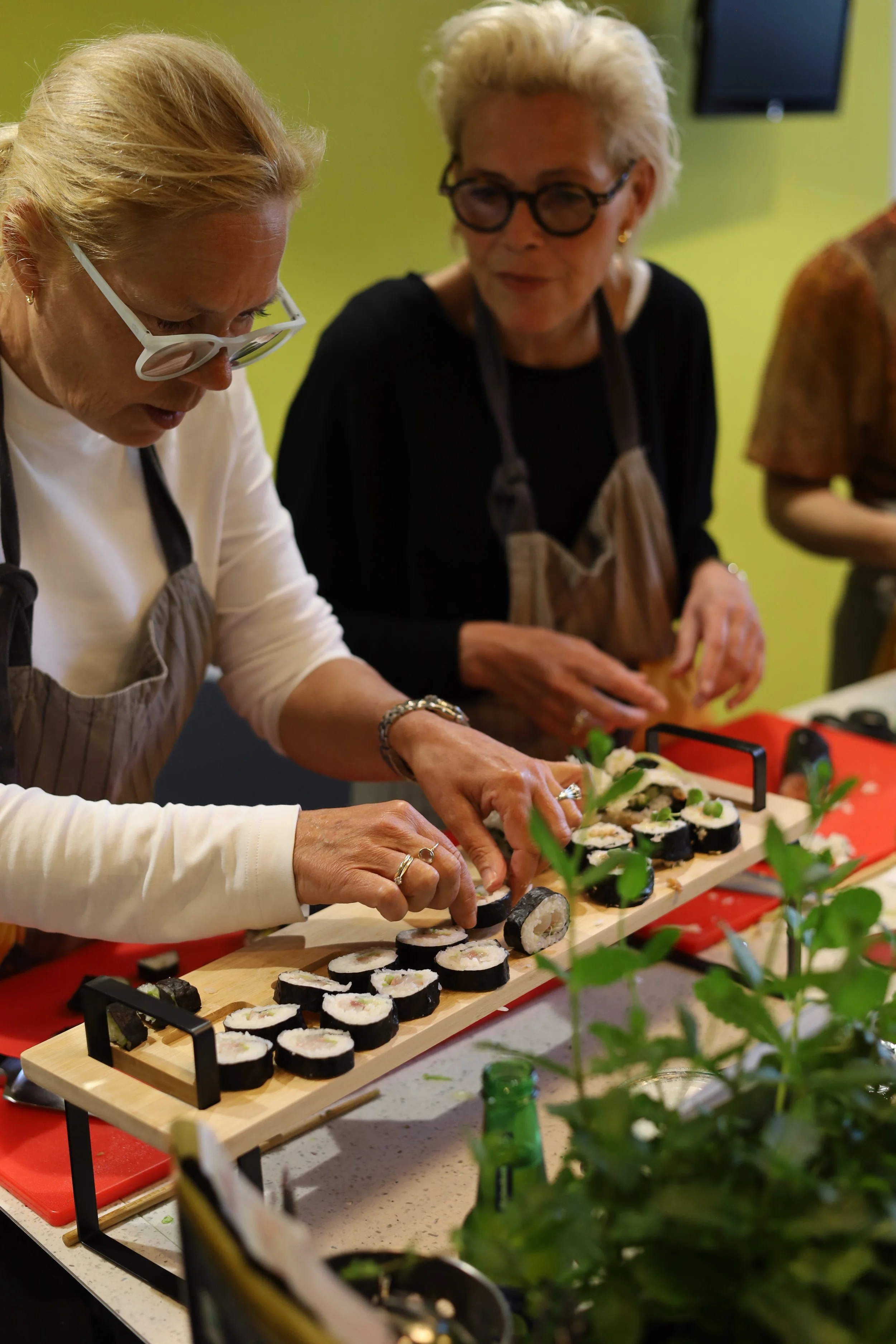 Vijf mensen maken sushi op een tafel met een groene achtergrond.