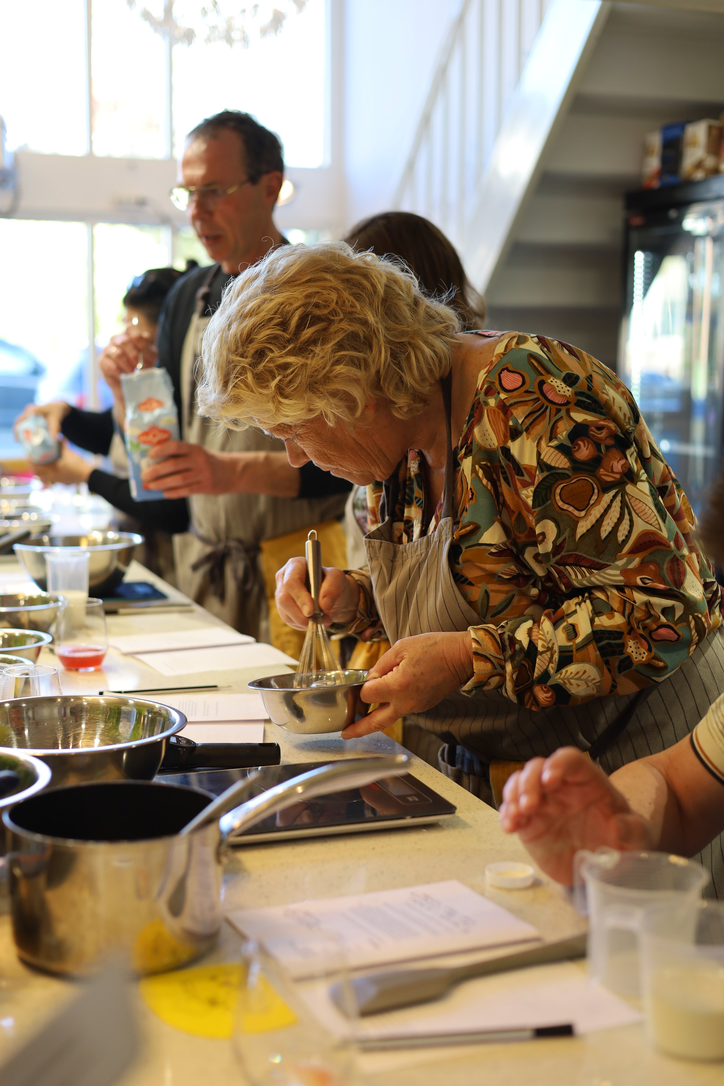 Mensen betrokken bij een kookworkshop in een keuken, met verschillende pannen en ingrediënten op de werkbladen.