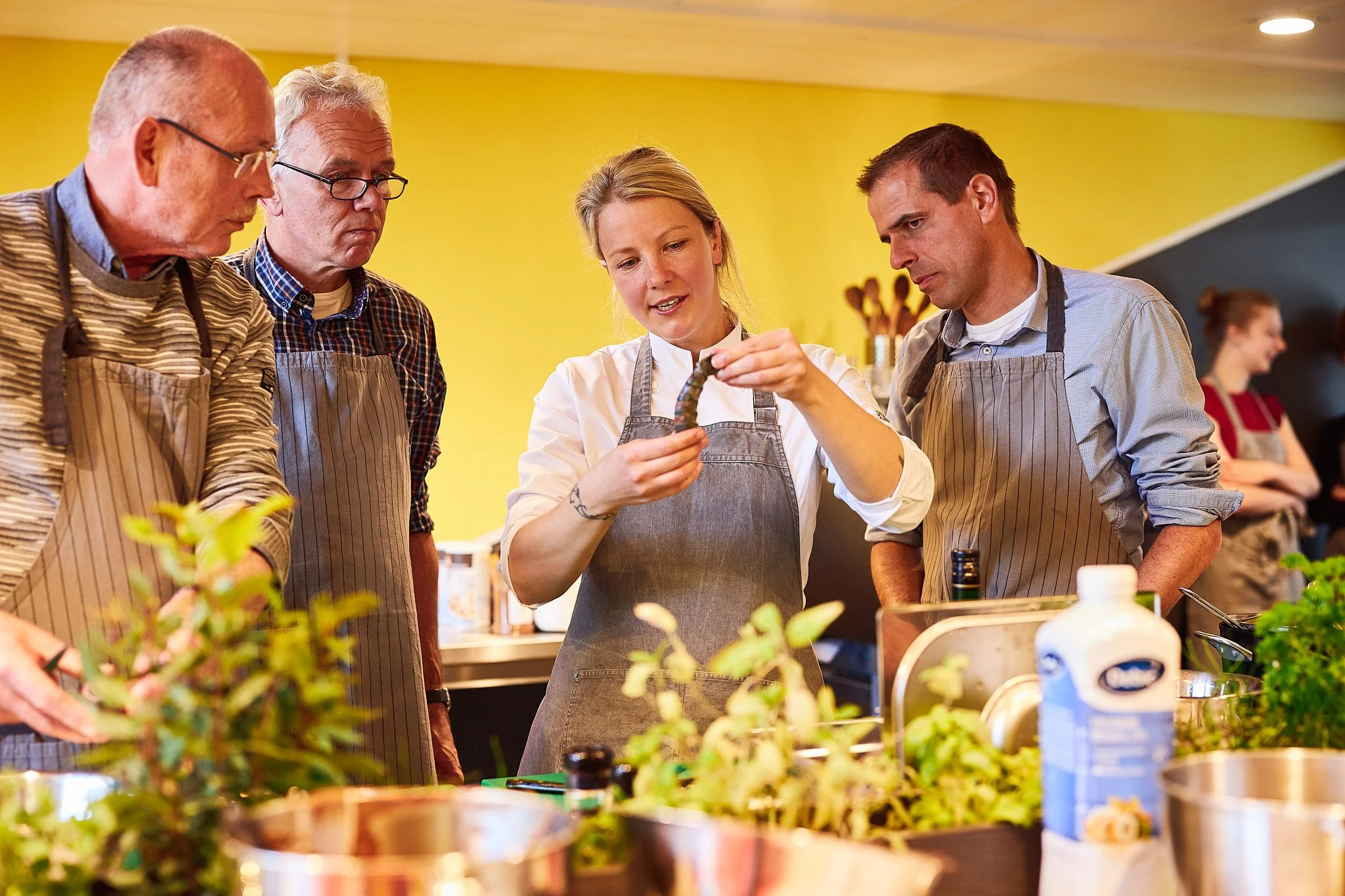 Een groep mensen in een keuken of kookstudio die samen iets bereiden, met groenten en kookgerei op de tafel.