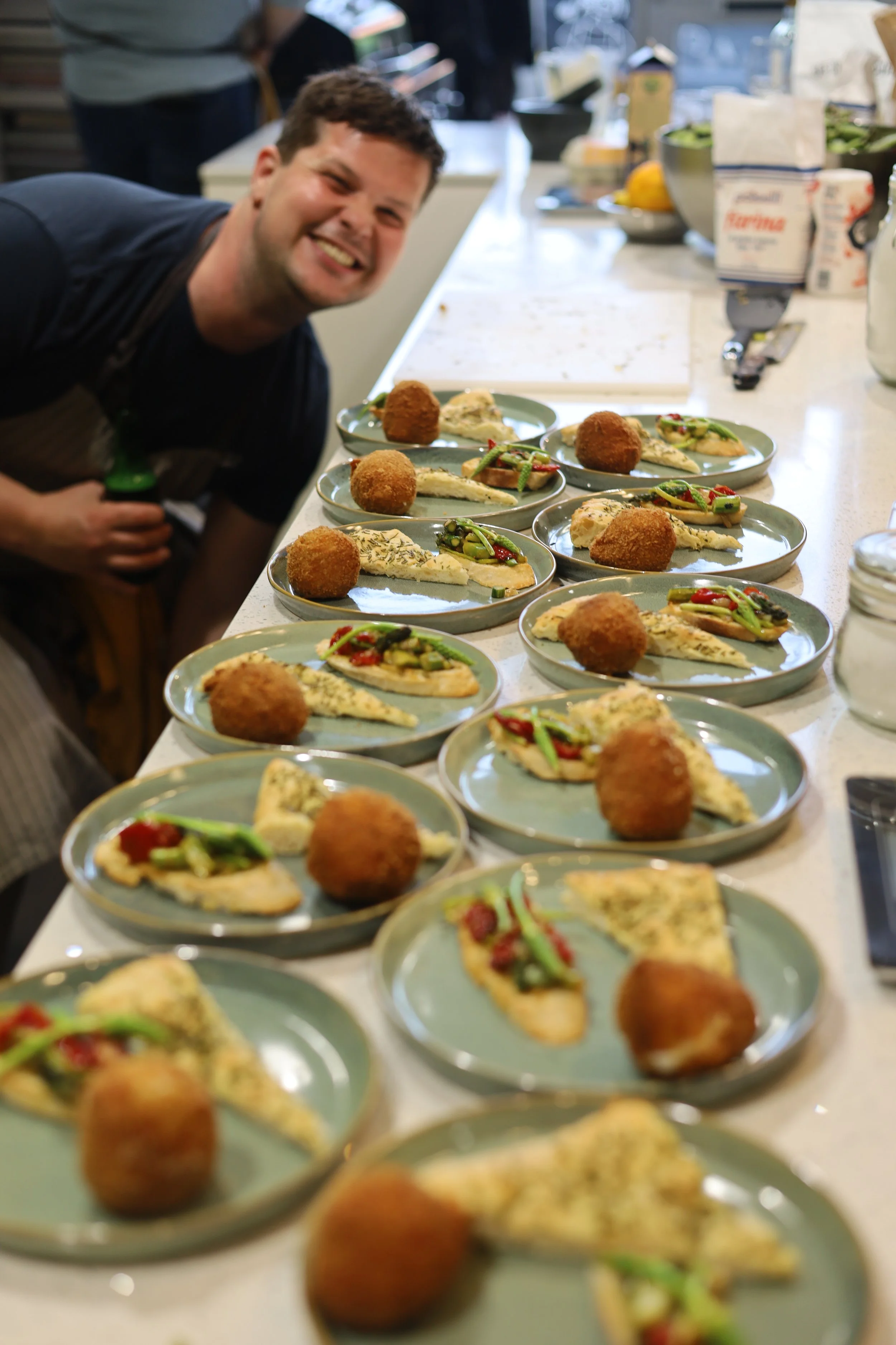 Man lachend voor meerdere borden met verschillende soorten eten op een keukenvoorgrond.