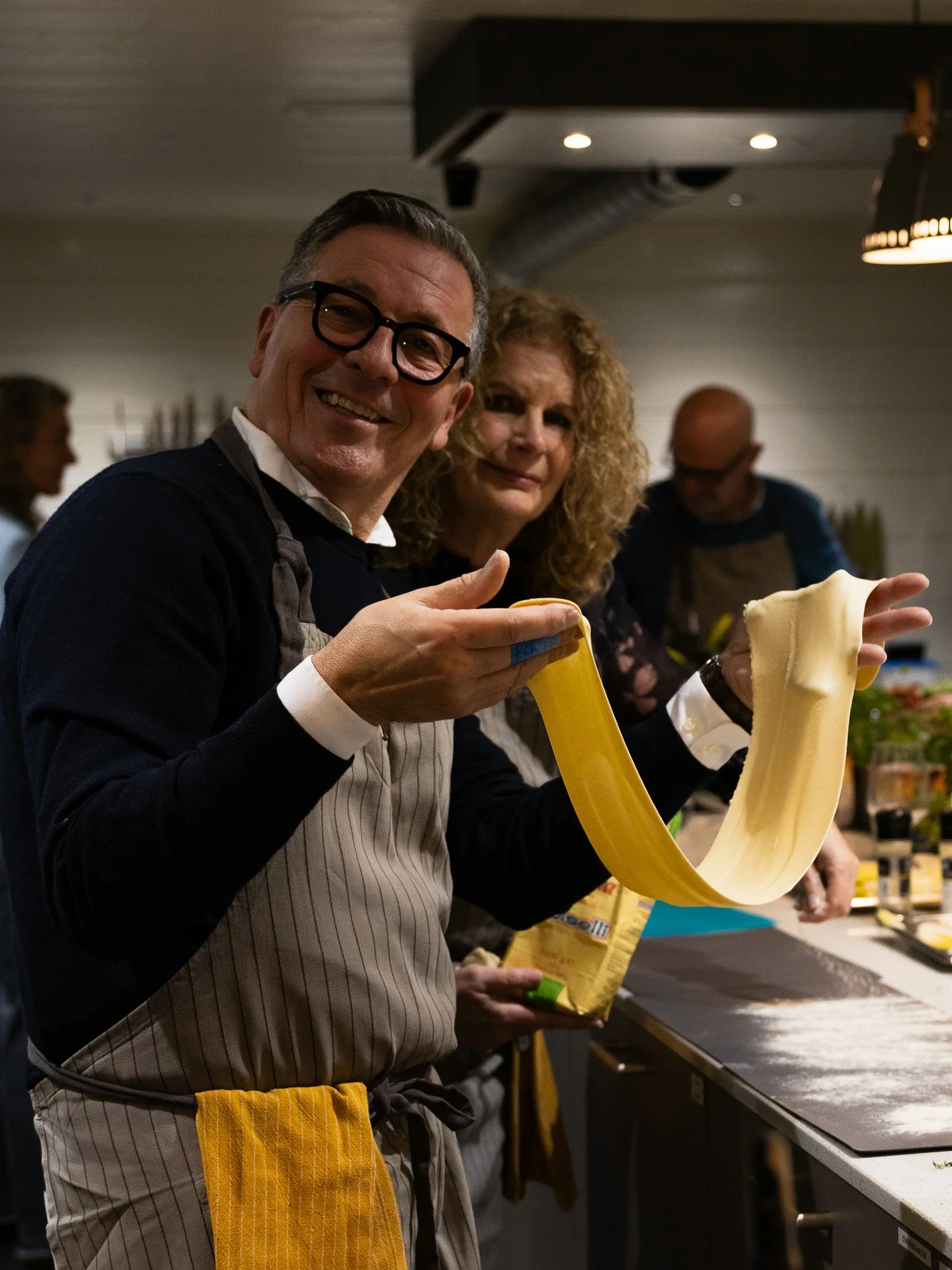 Mensen maken pasta in een keuken, met een grote sliert deeg die wordt uitgerekt en gesneden.