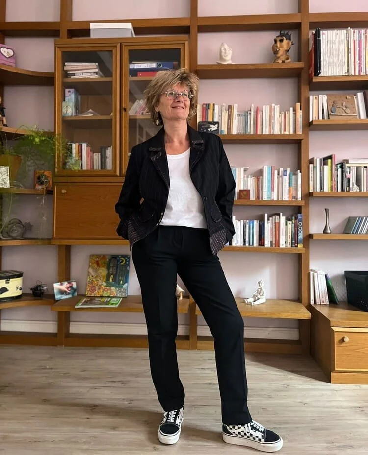 Une femme debout dans un salon avec des étagères contenant des livres et des décorations en arrière-plan.