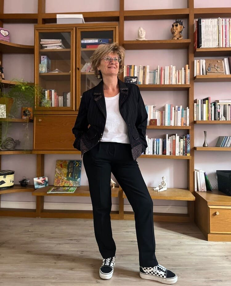 Une femme debout dans un salon avec des étagères contenant des livres et des décorations en arrière-plan.
