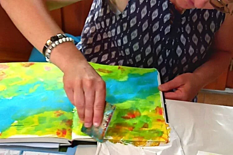 Une personne en robe à motifs peignant un livre d'illustrations avec des couleurs vives.