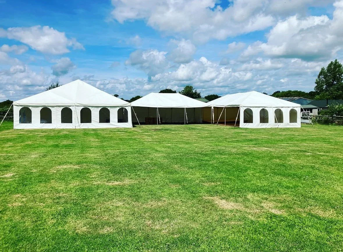 Three large white outdoor party tents on a grassy field under a partly cloudy sky.