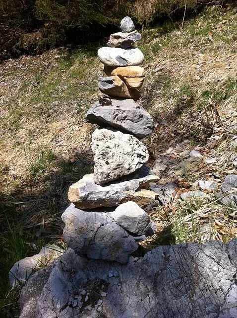 Stacked rocks balanced vertically outdoors on a grassy and rocky terrain.