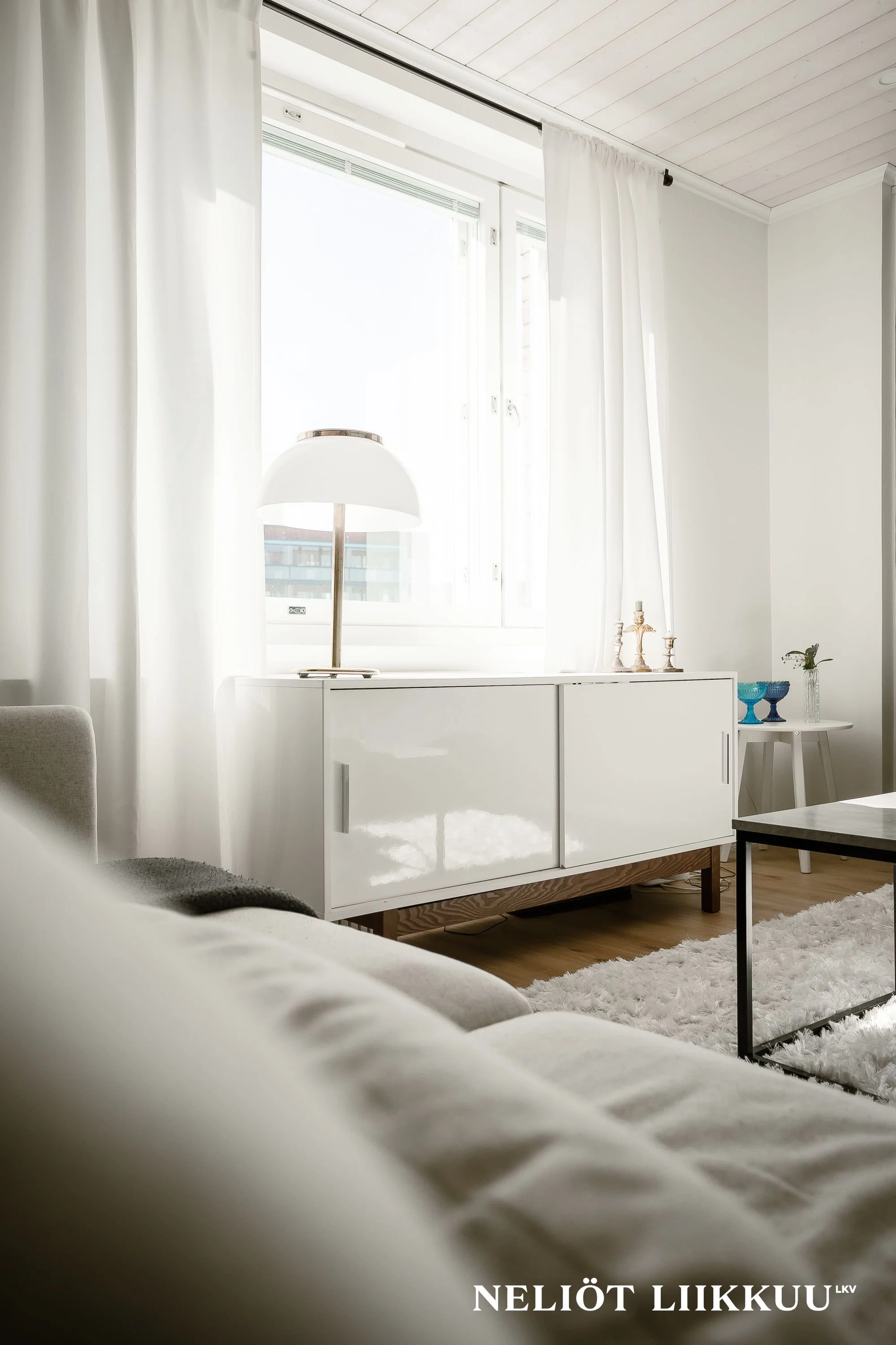 Olohuone, jossa paljon vaaleita värejä, iso ikkuna ja sohva