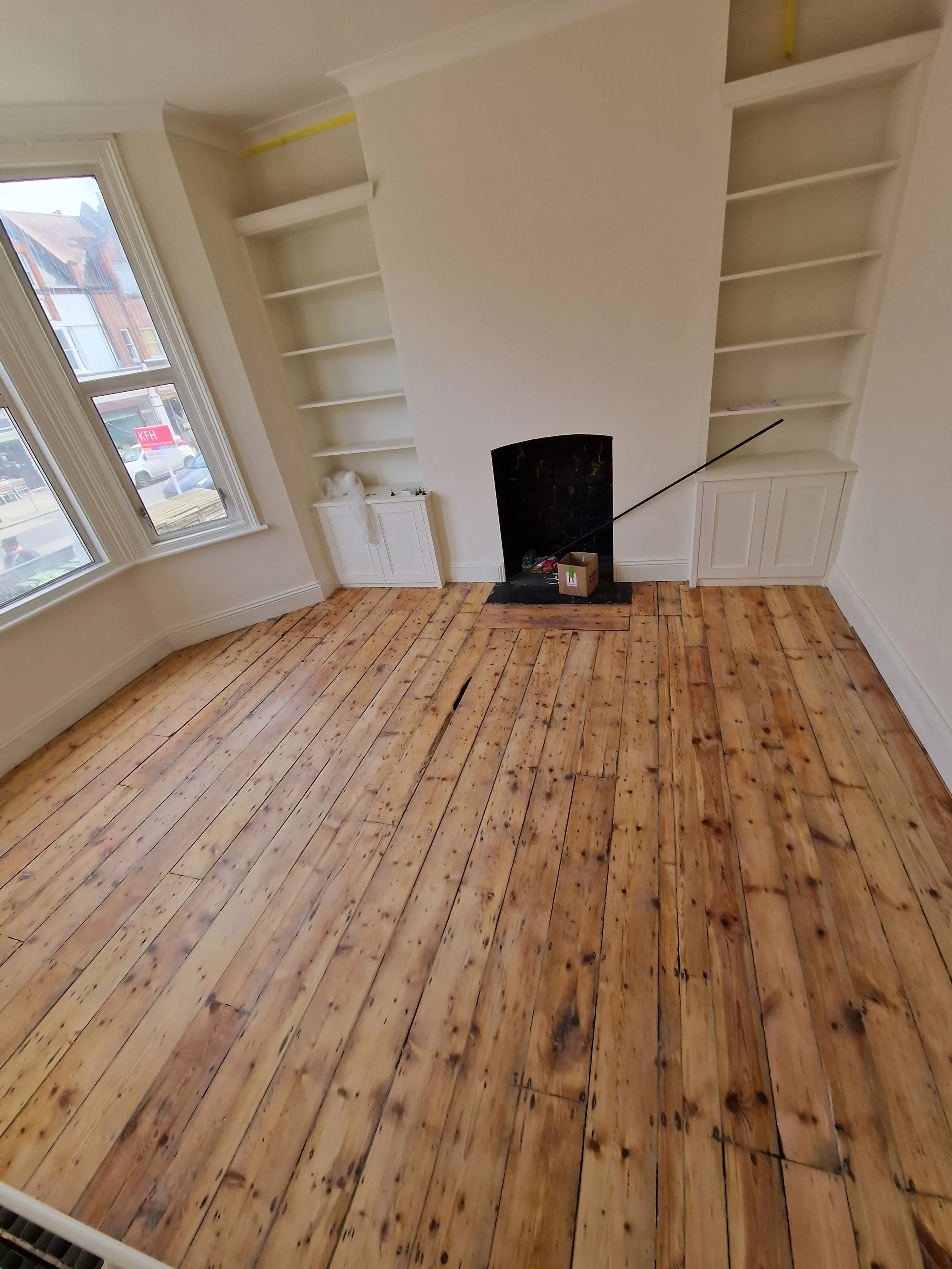 Empty room with large windows, wooden floor, and built-in white bookshelves surrounding a fireplace.