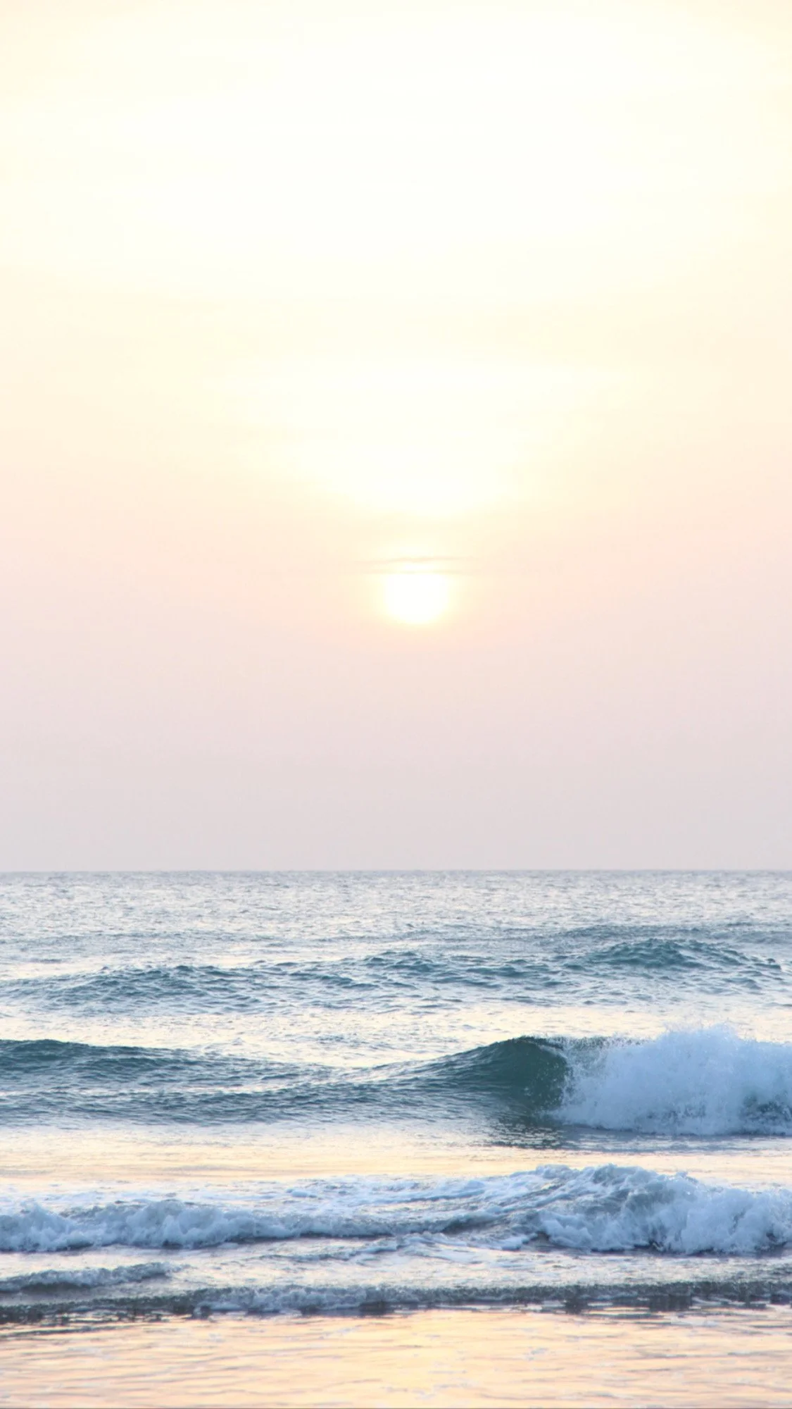 Sonnenuntergang über dem Meer mit Wellen im Vordergrund.