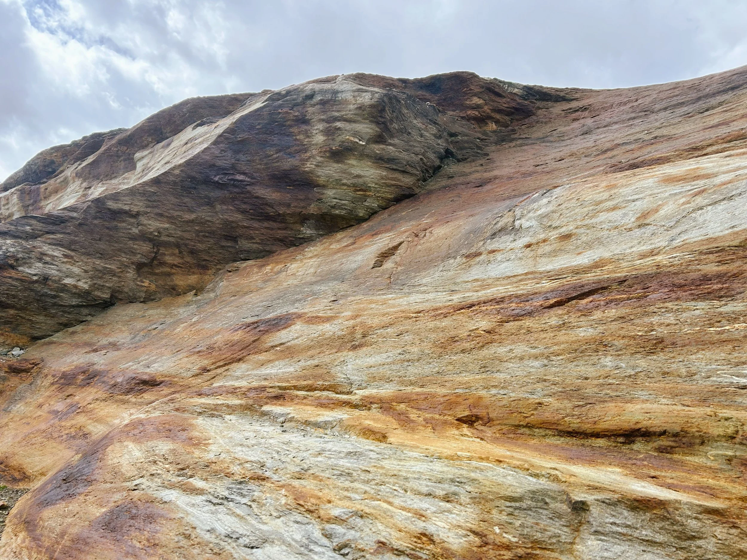 Nahaufnahme eines Felsen mit bunten Schichten in der Natur, Himmel mit Wolken im Hintergrund.