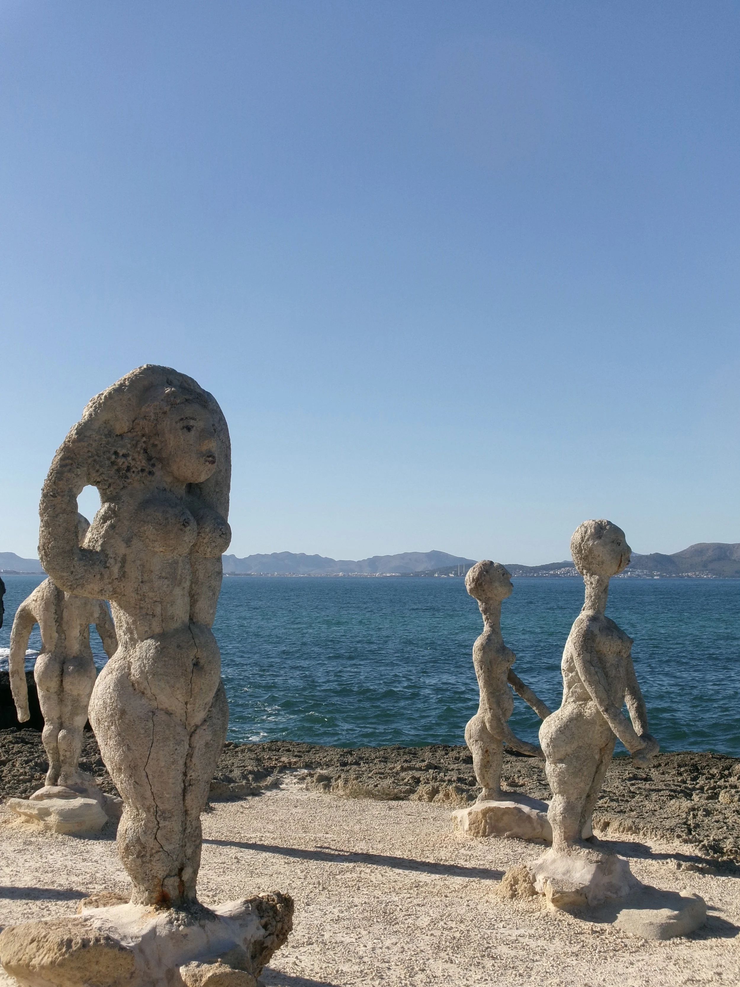 Säulen aus Steinen, die menschliche Figuren darstellen, stehen am Ufer eines Sees mit Bergen im Hintergrund