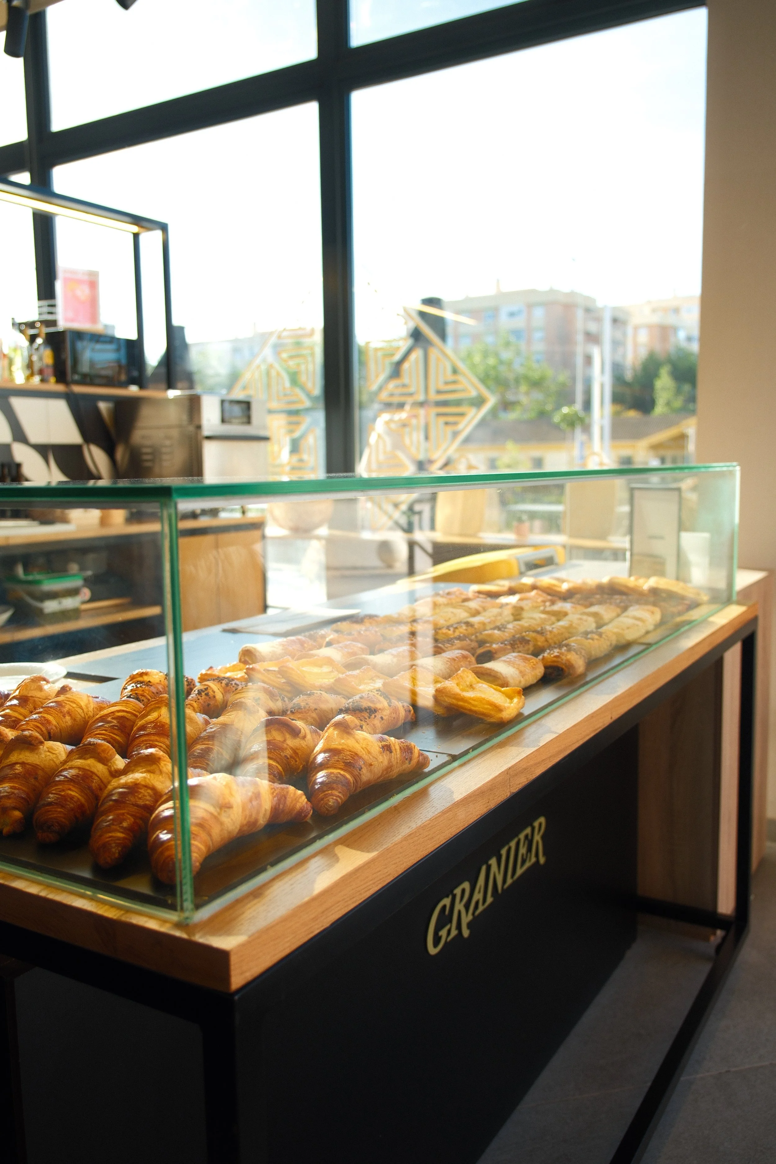 Display case filled with croissants in a bakery cafe with large windows and a view of buildings outside.