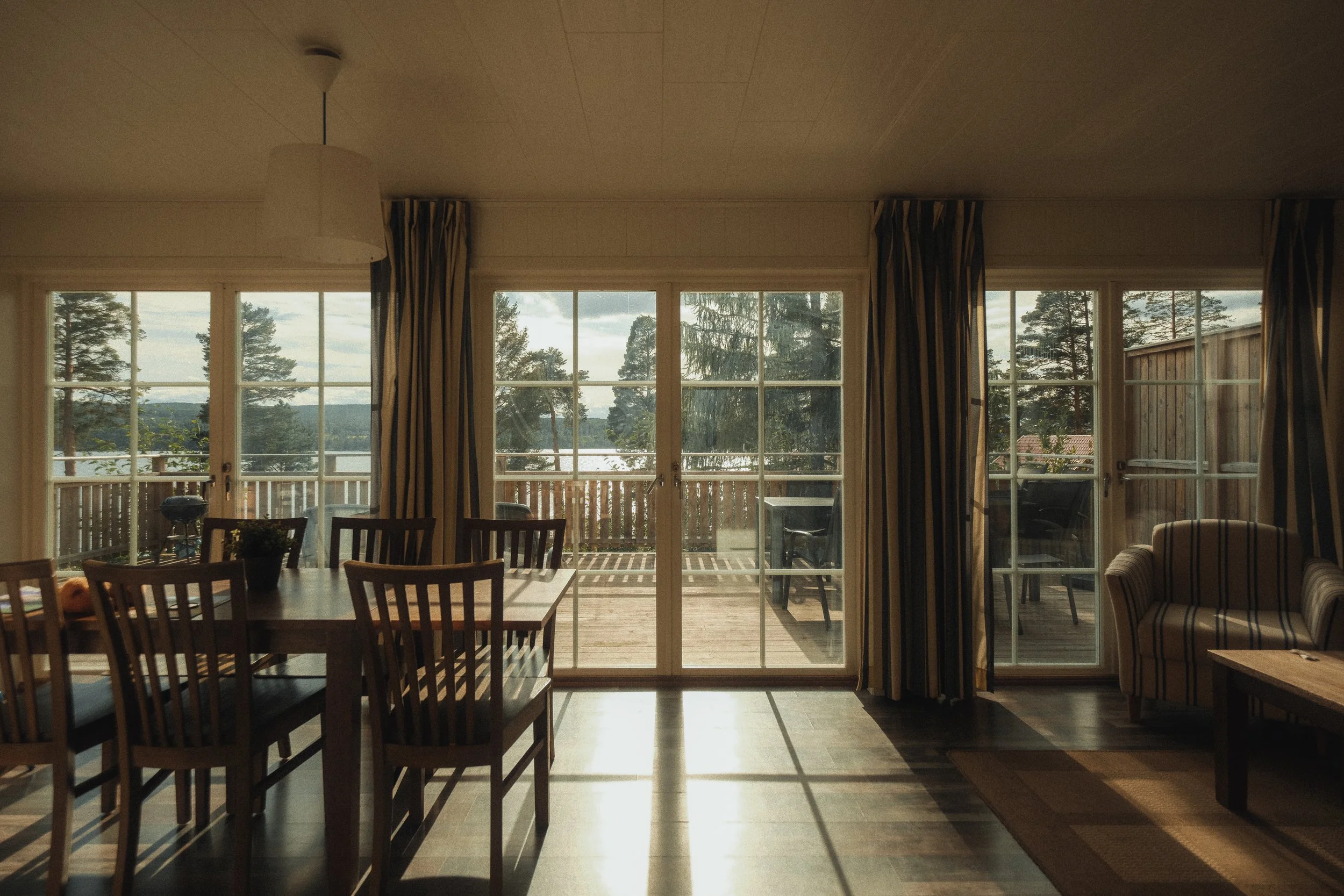 Living room with large glass sliding doors overlooking a deck with outdoor furniture and view of trees and water, daytime