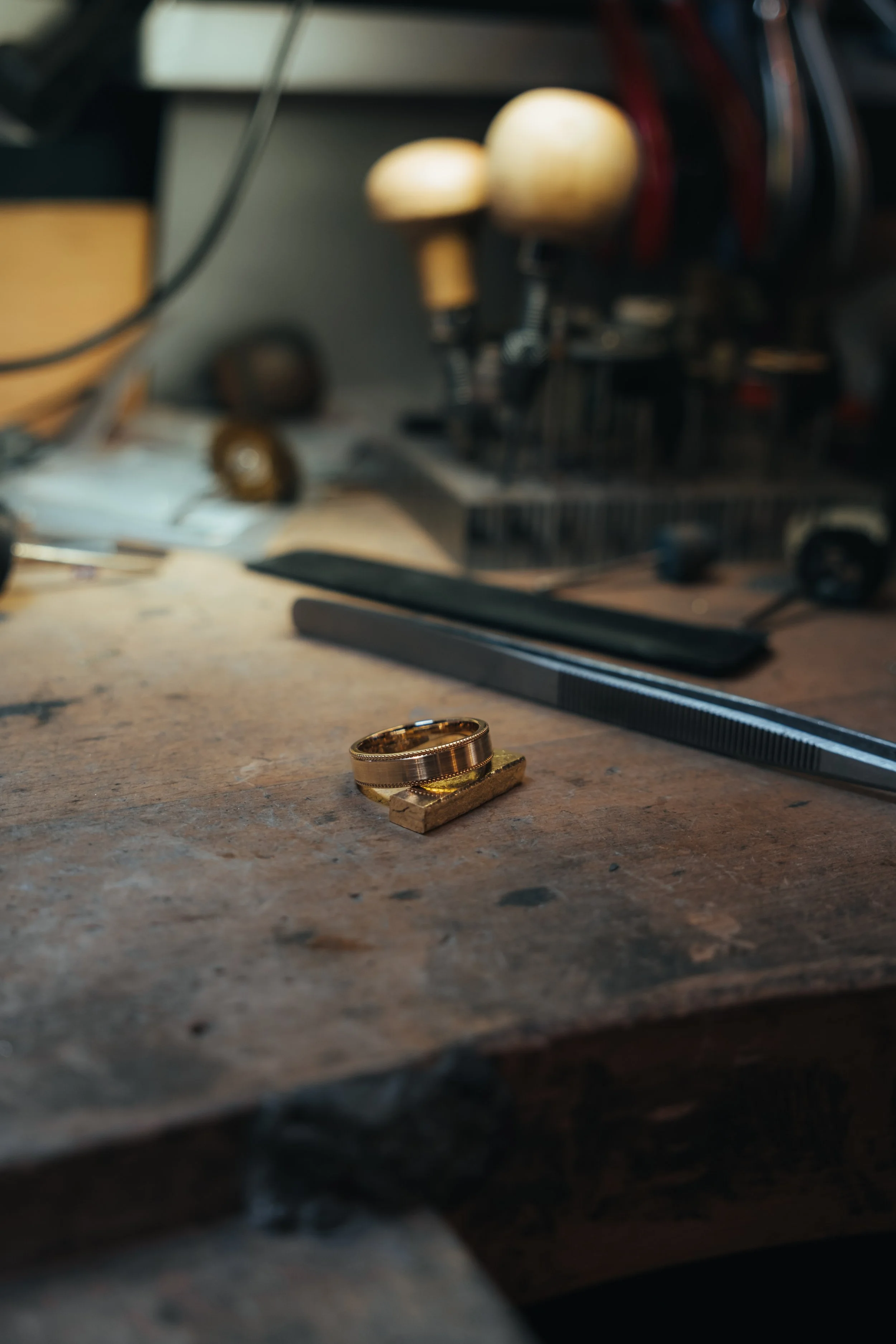 Close-up of a multi-layered gold ring on a workbench with tools and machinery in the background.