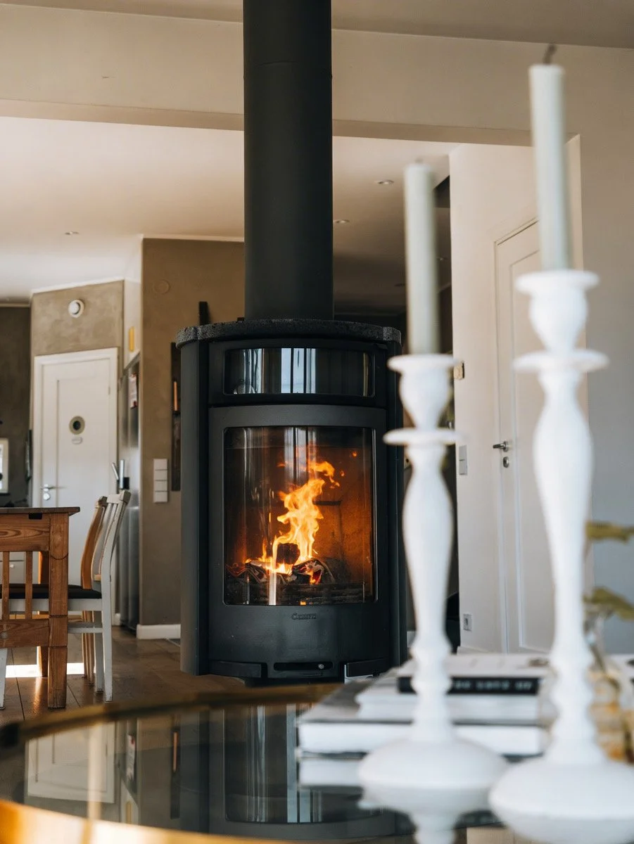 A modern home interior with a black wood-burning stove and visible flames, surrounded by decor including a white candelabra and books.