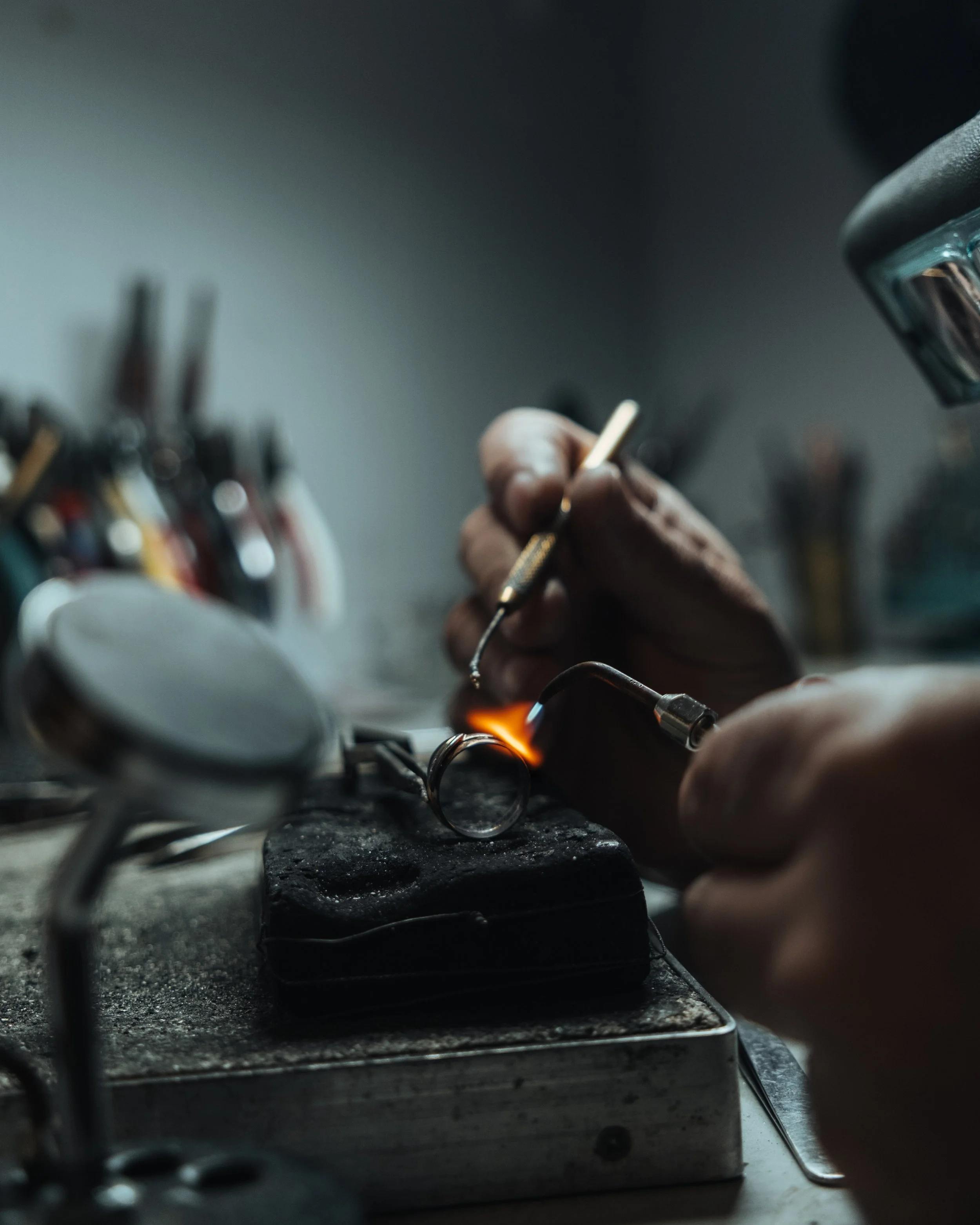 Close-up of a person soldering a small metal piece with a soldering iron, with wires and equipment nearby.