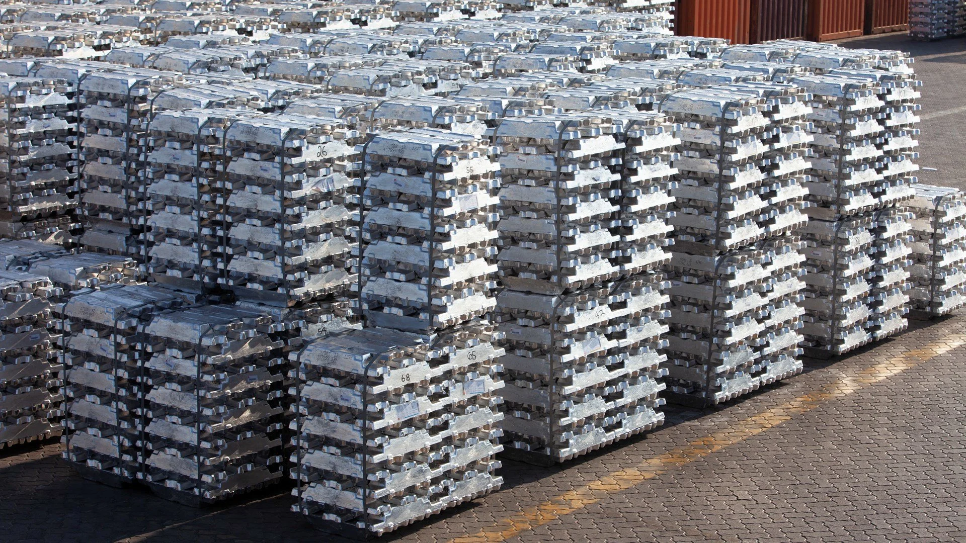 Stacks of aluminum ingots secured on pallets at a storage yard.