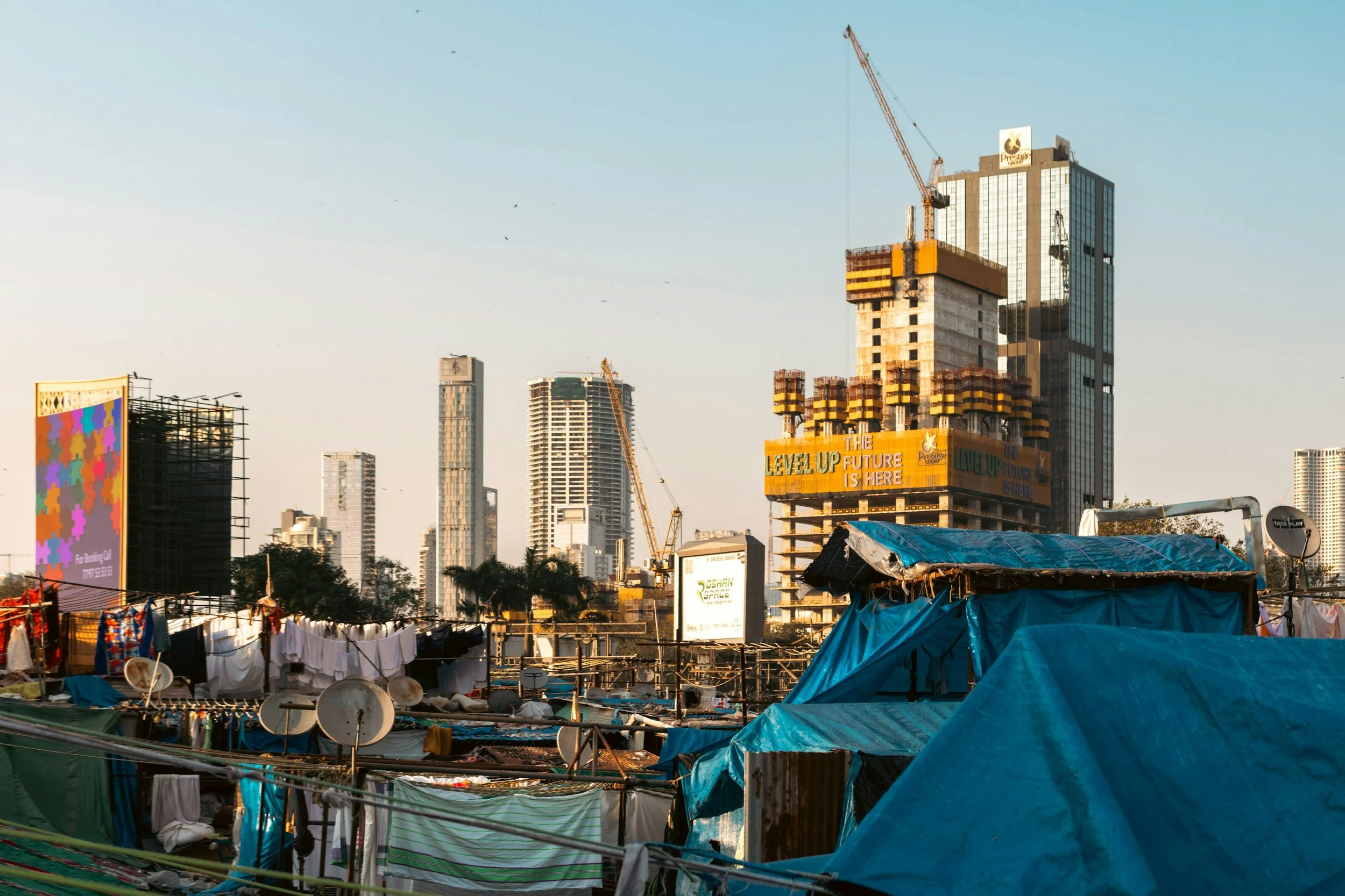 Comércio de roupas e cabanas de toca em primeiro plano, na cidade de novos edifícios altos ao fundo, durante o dia.