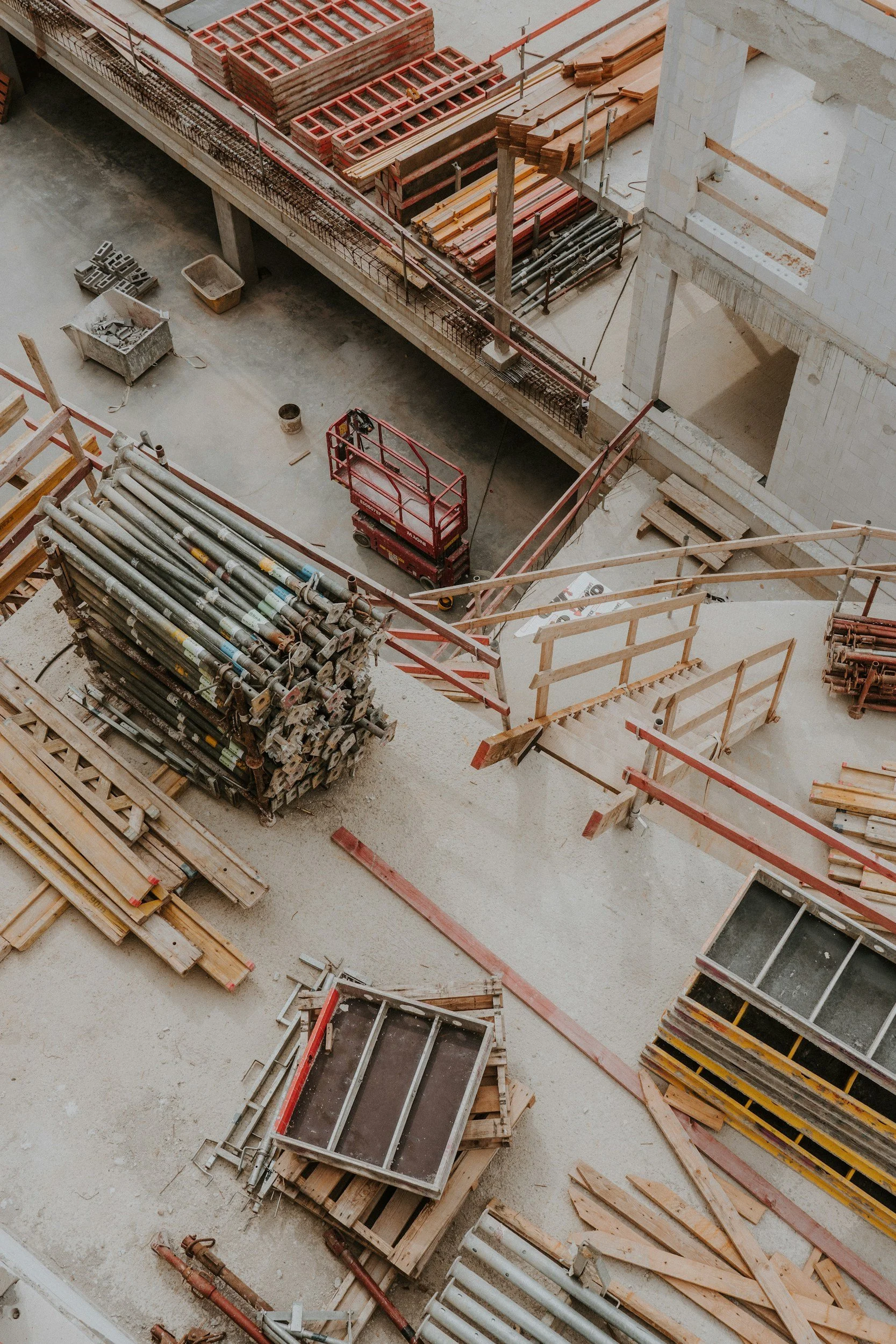 Imagem de um canteiro de obras com materiais de construção, andaimes e equipamentos de construção em uma estrutura de prédio em construção.